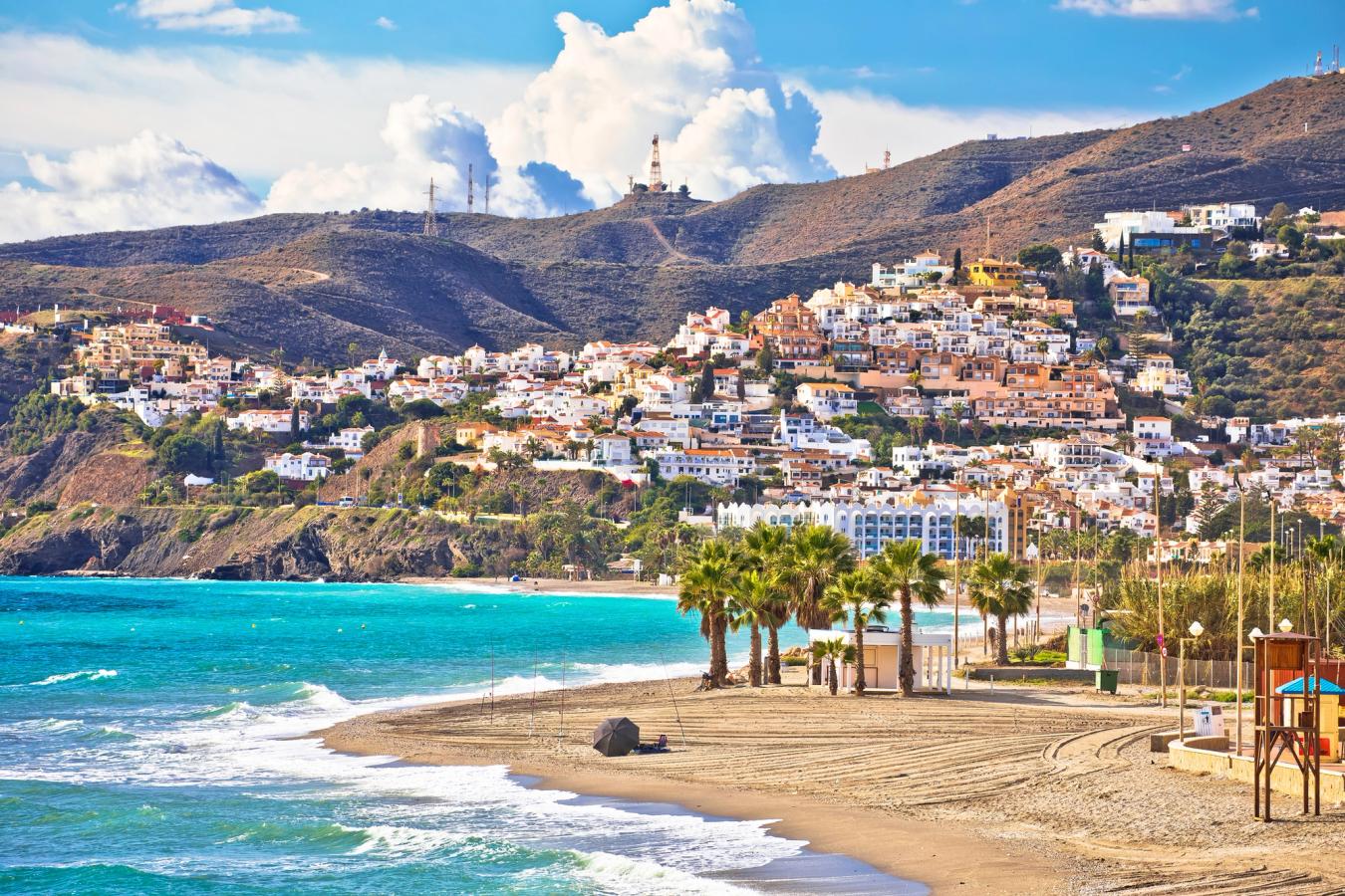 Utsikt til de hvitklalkede husene i Nerja med turkis vann og nydelig sandstrand med fjellene i horisonten