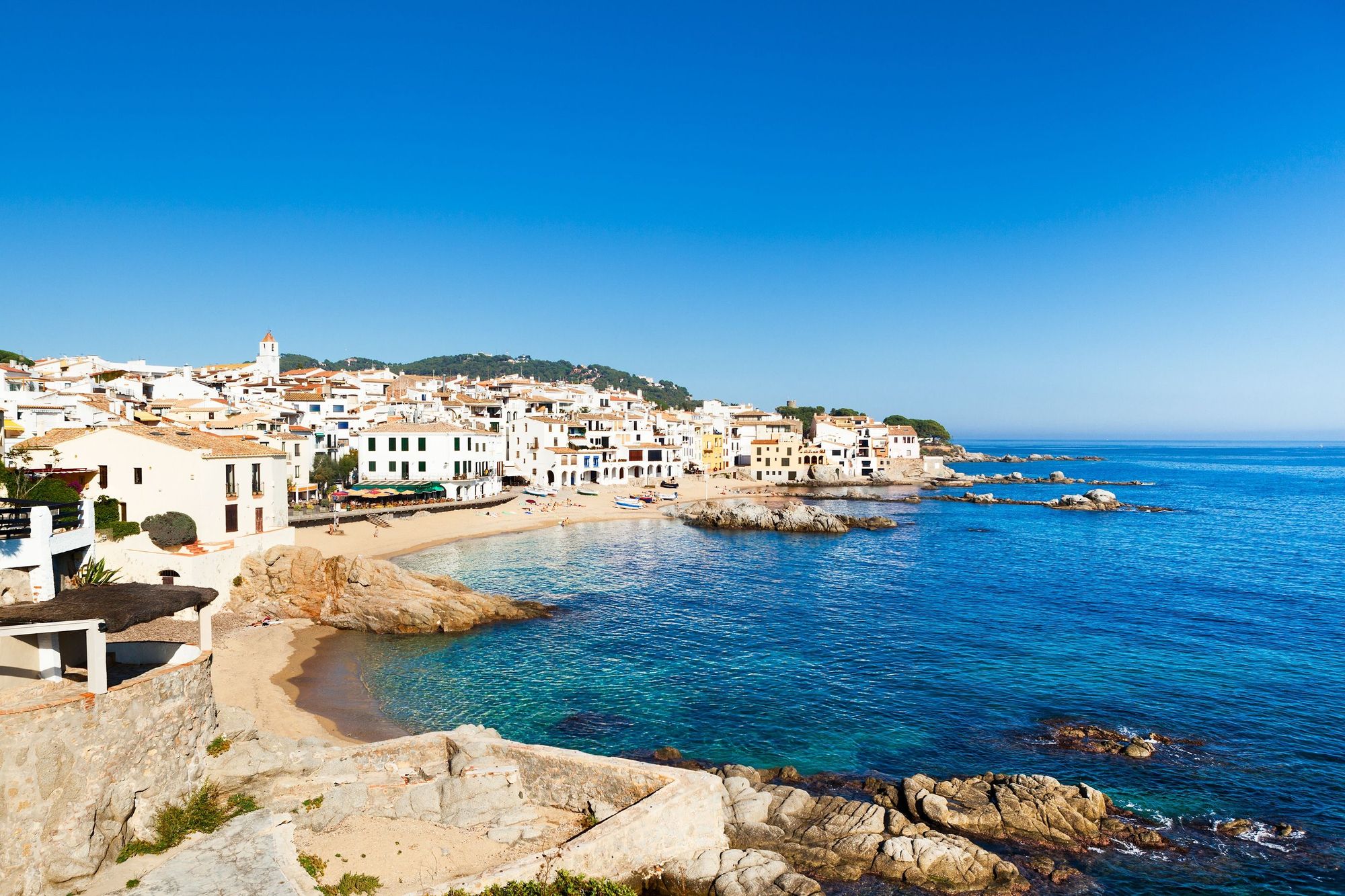Utsikt over Calella de Palafrugell med en liten sandstrand og hvitkalkede hus langs vannkanten ved det krystallklare havet