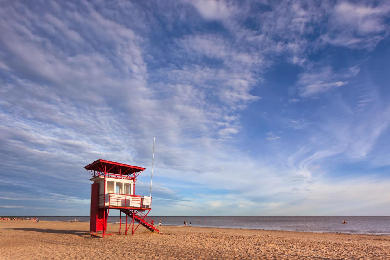 Bilden visar den breda sandstranden i Pärnu med ett rött livräddartorn i mitten av bilden