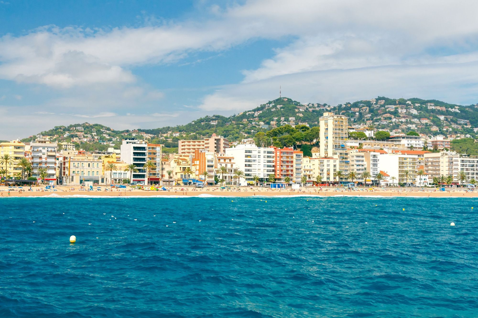 Utsikt fra havet mot stranden i Lloret de Mar og fjellene i bakgrunnen på Costa Brava i Spania