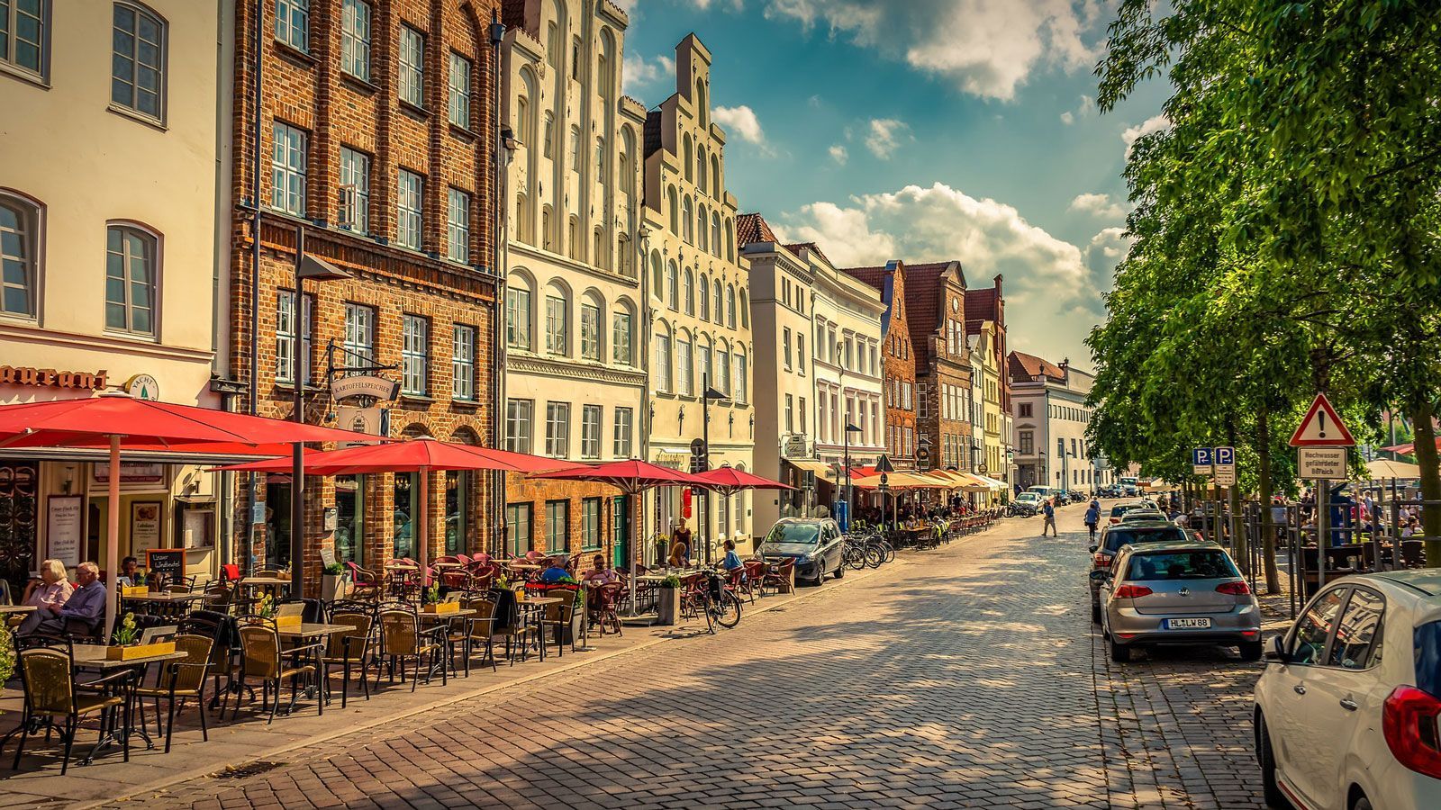 Bildet viser en koselig brosteinsbelagt gate i Lübeck med fortauskafeer og sammenhengende hus. 