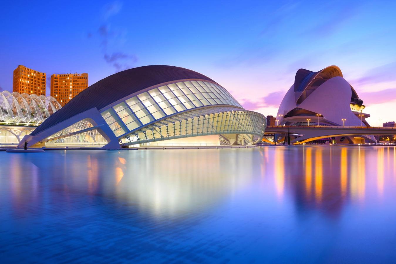 Billedet viser den unikke arkitektur i Ciudad de las Artes y las Ciencias i Valencia. Den kendetegnes af de enorme støbte buegange og vandspejlene, der omkranser dem.