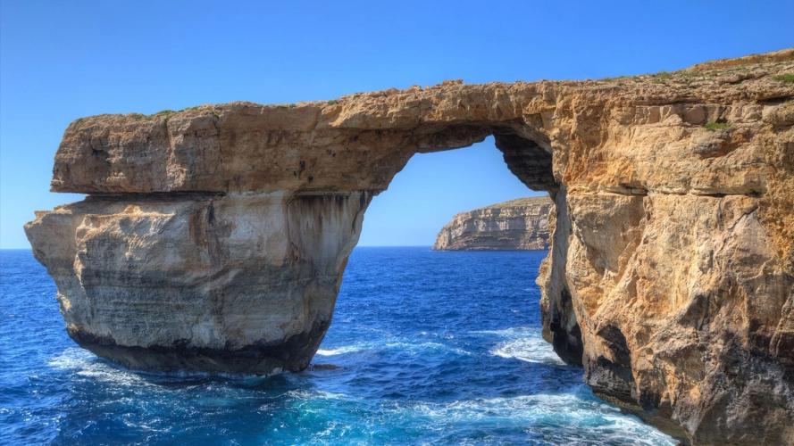 Over det kongeblåe havet er en naturlig kalksteins bue man igjennom kan se havet fortsette til andre klipper i bakgrunnen