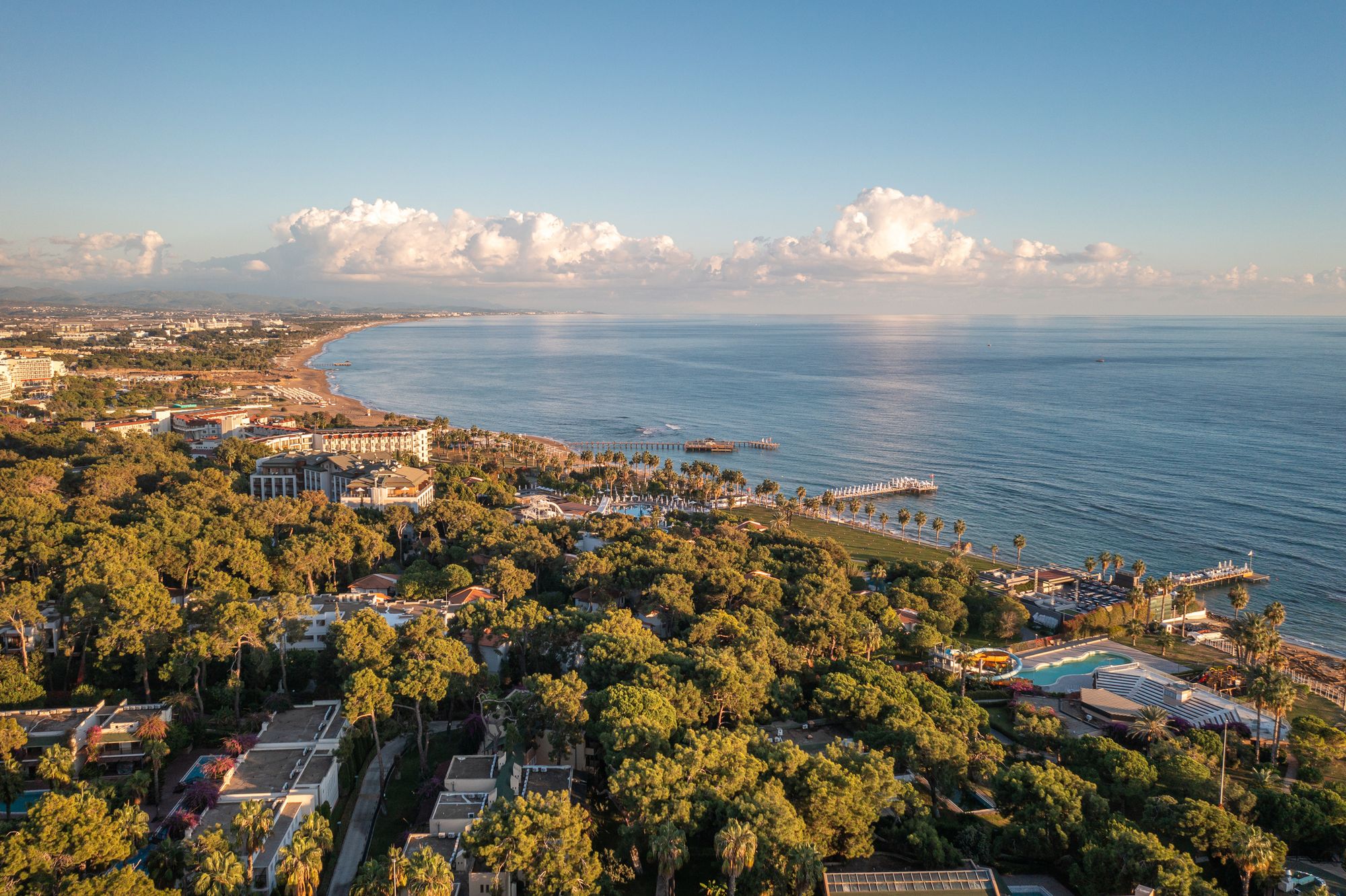 Kystlinjen ved Titreyengol i Tyrkiet er præget af hoteller, der ligger ud mod havet og stranden, omgivet af en masse træer. I horisonten hænger et lavt skydække over fastlandet og havet.