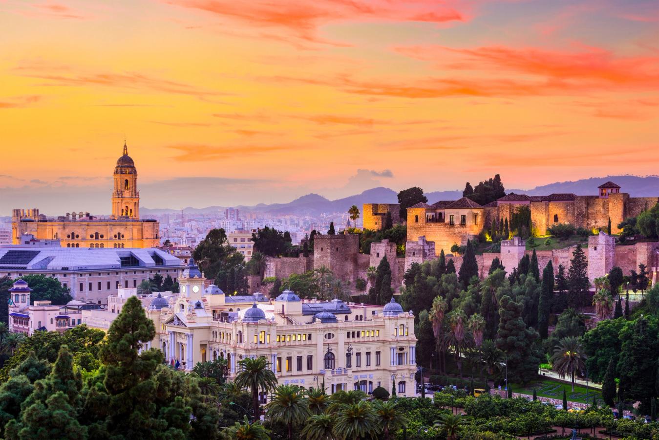 Middelalderslottet Alcazaba til høyre sammen med rådhuset i midten, og katedralen i Malaga til venstre. Alt under lyset fra en solnedgang.