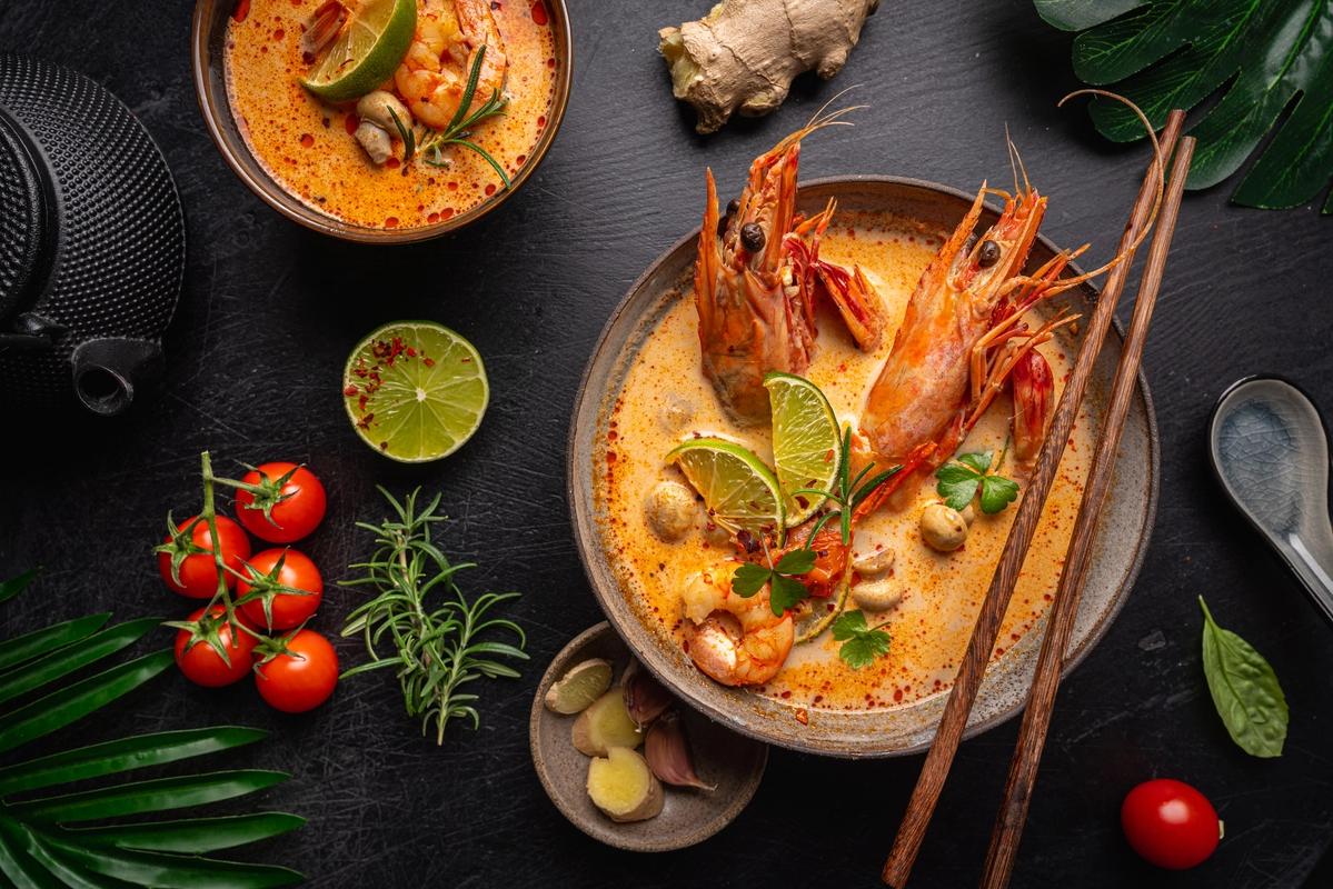 Bildet viser to skåler med den kjente suppe-retten Tom Yum Goong. Suppen er av rødlig farge med store reker i. Rundt skålene ligger ulike små grønnsaker, skjeer og spisepinner.