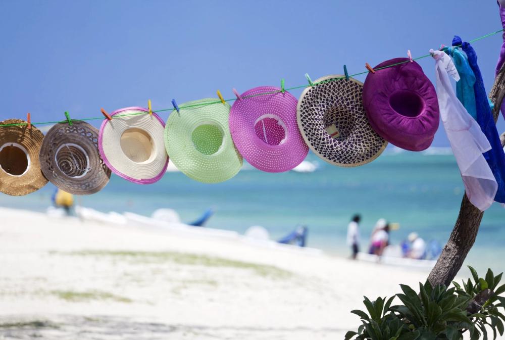 Färgglada solhattar hänger på en tvättlina vid stranden i Flic en Flac, Mauritius, med det turkosblå havet och den vita sanden i bakgrunden.