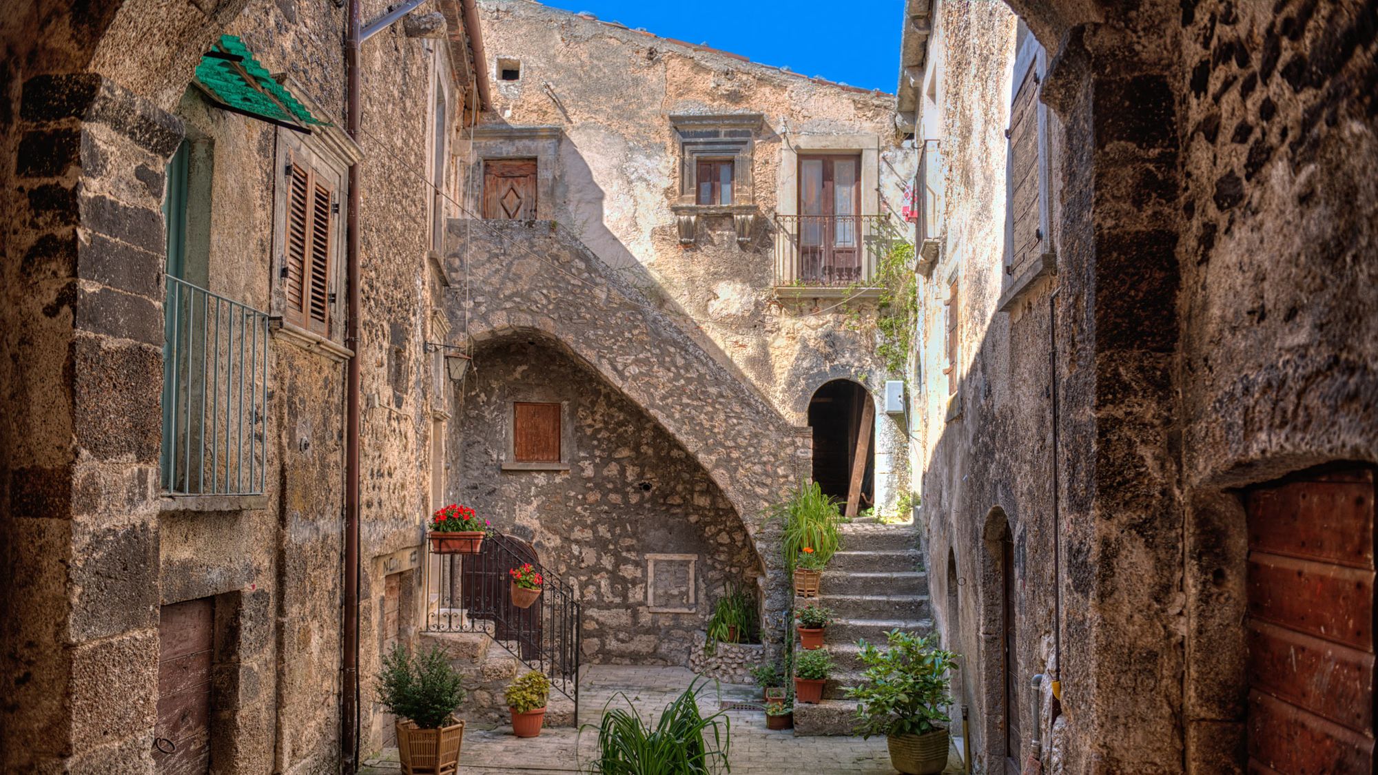 Kullstensgata och liten torg med blommor och trappor i Santo Stefano di Sessanio i Abruzzo