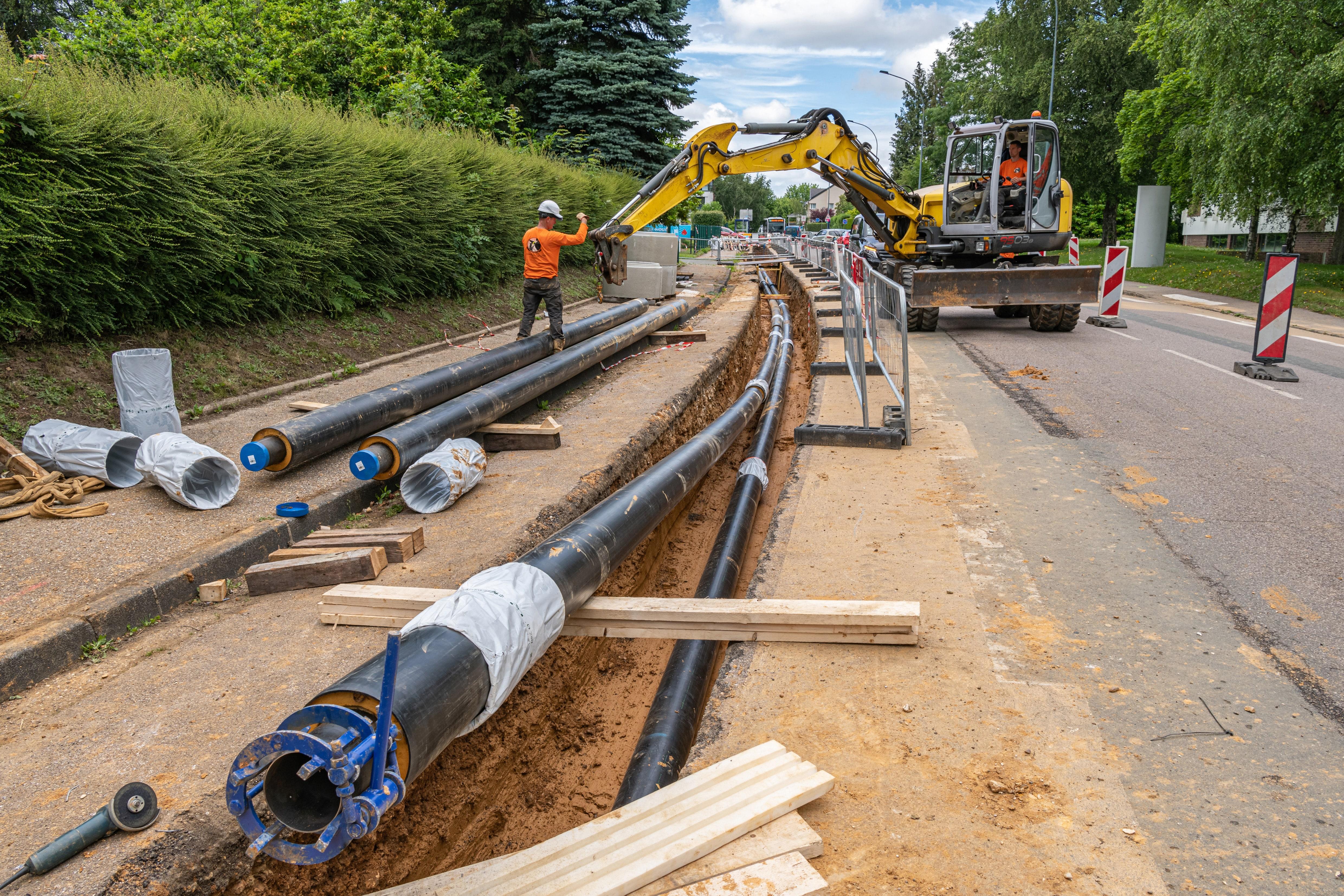 Chantier de pose de canalisations d'un réseau enterré le long d'une voie, avec ouvriers et pelle mécanique