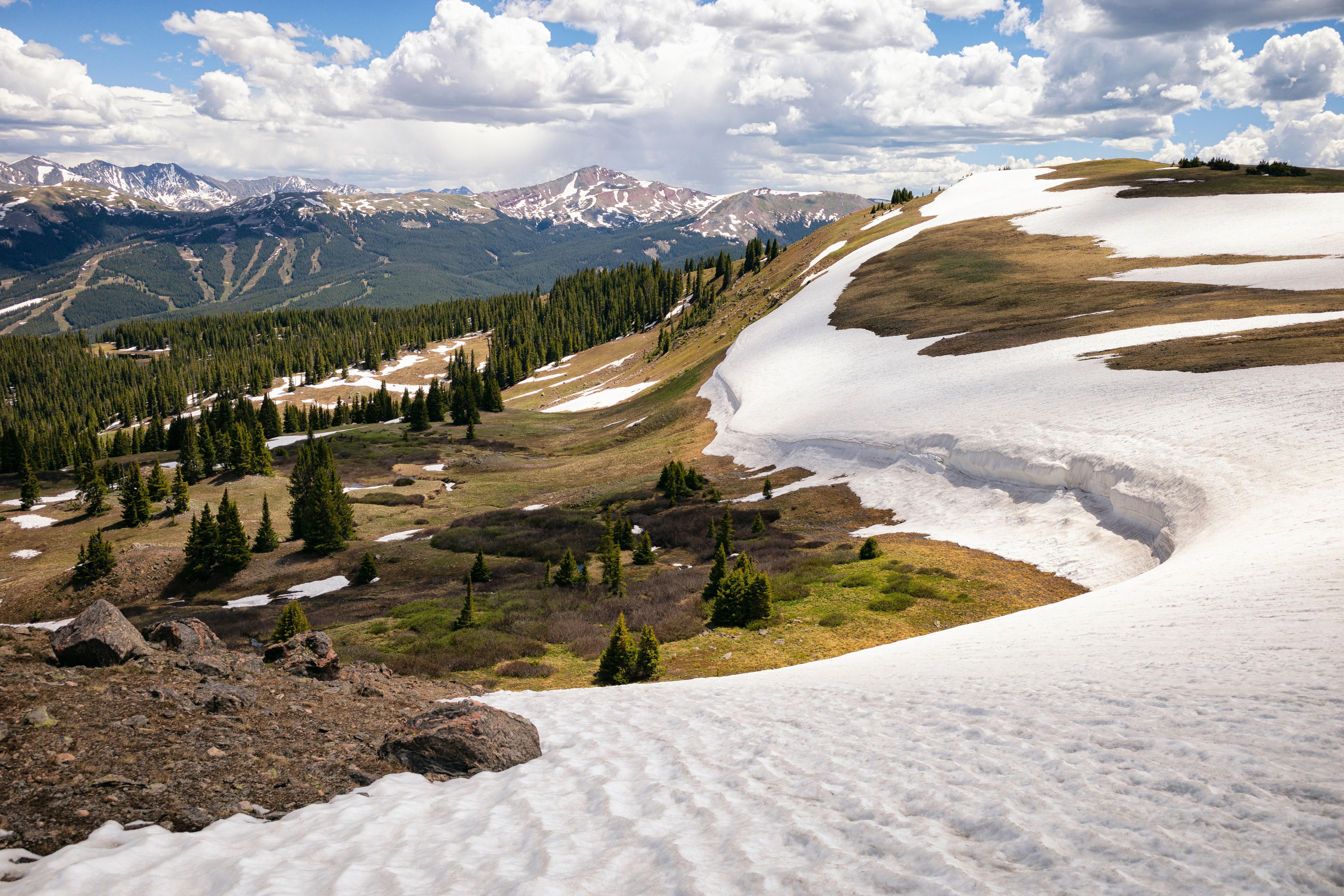 Paysage de haute montagne au printemps avec névés, alpages verdoyants et chaîne de montagnes en arrière-plan