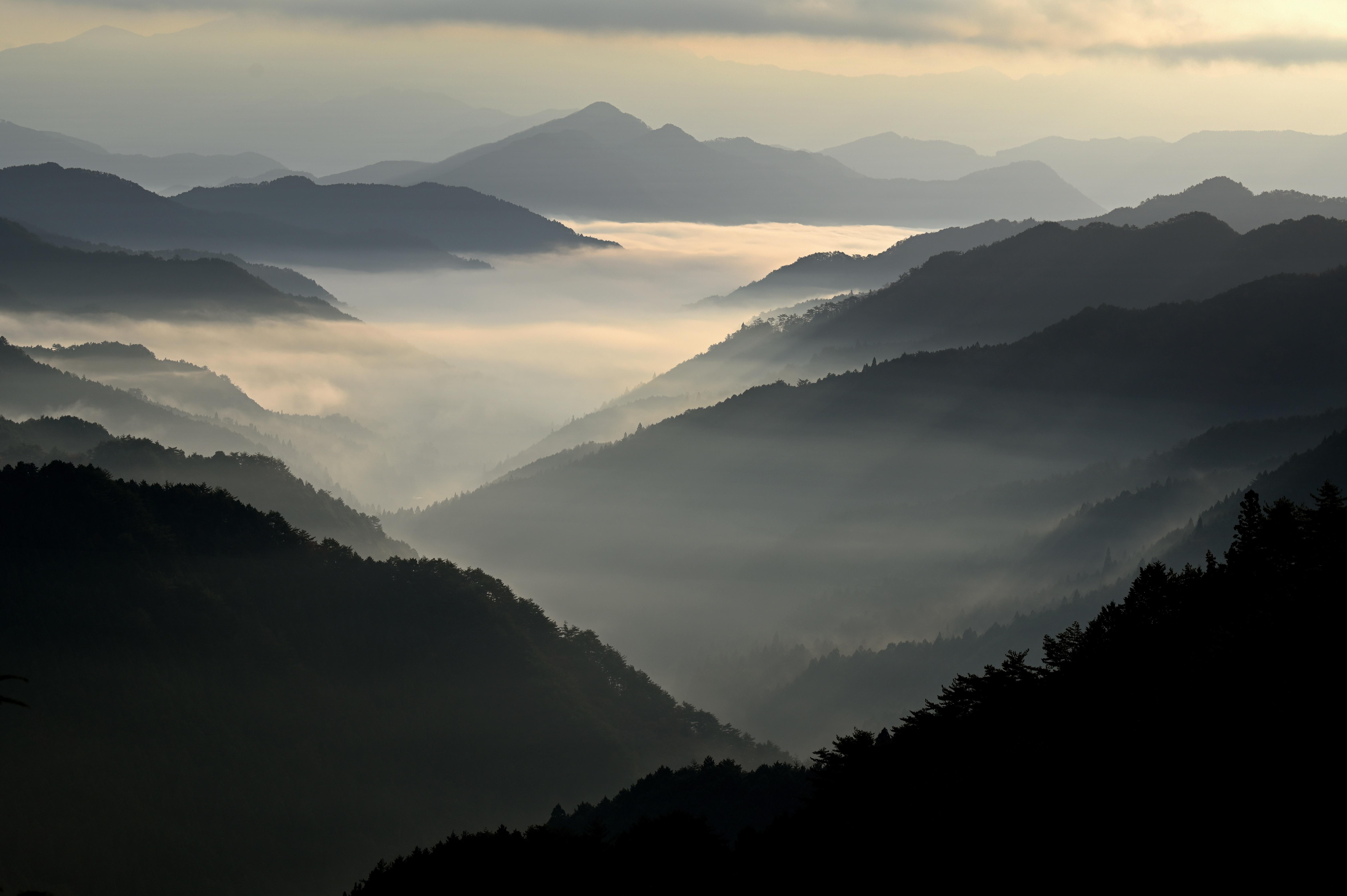 Paysage de montagnes successives noyées dans la brume au lever du jour, avec couches de nuages dans les vallées
