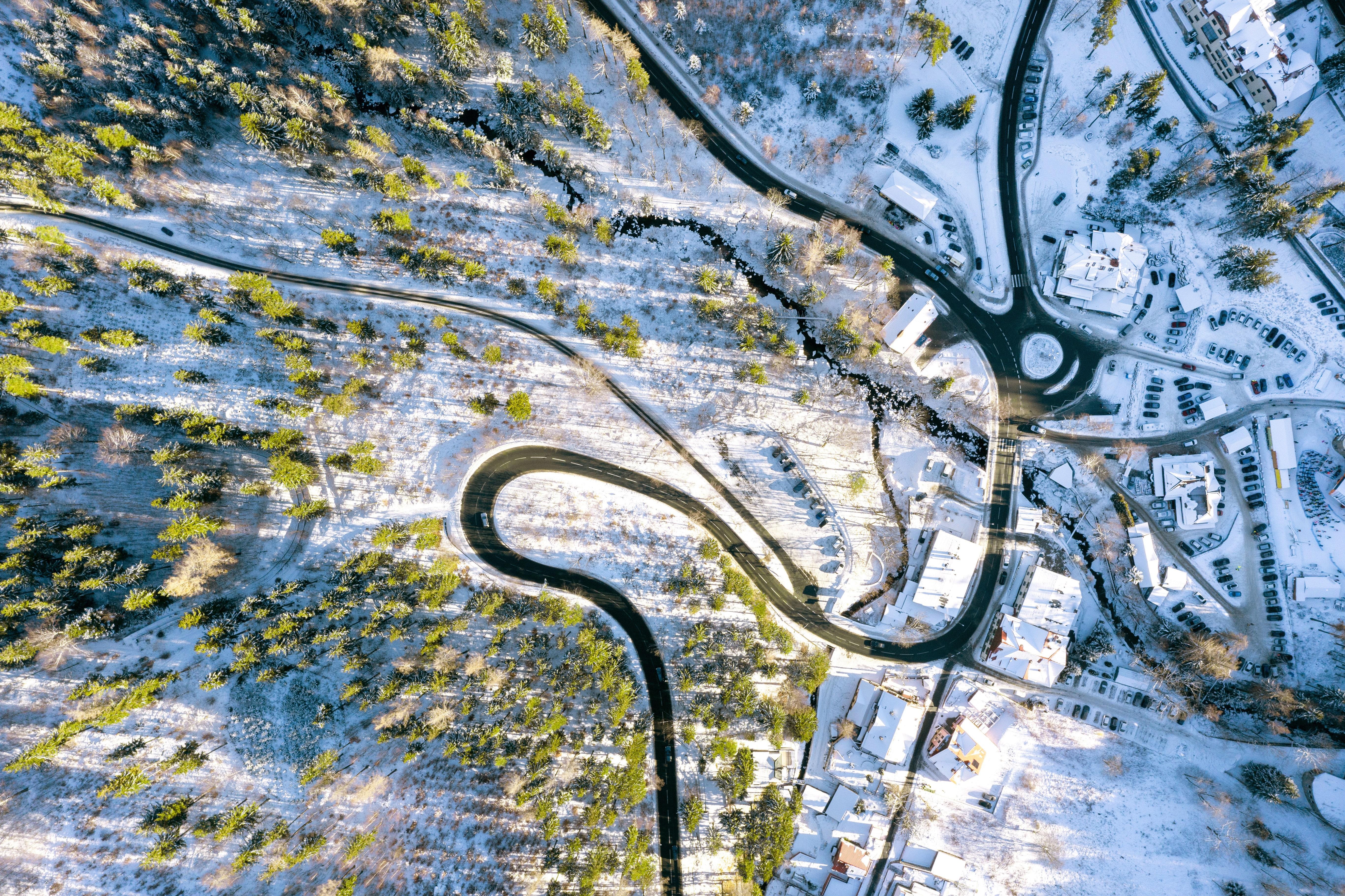 Vue aérienne en hiver d'une route sinueuse traversant un paysage enneigé, entre forêts et hameaux