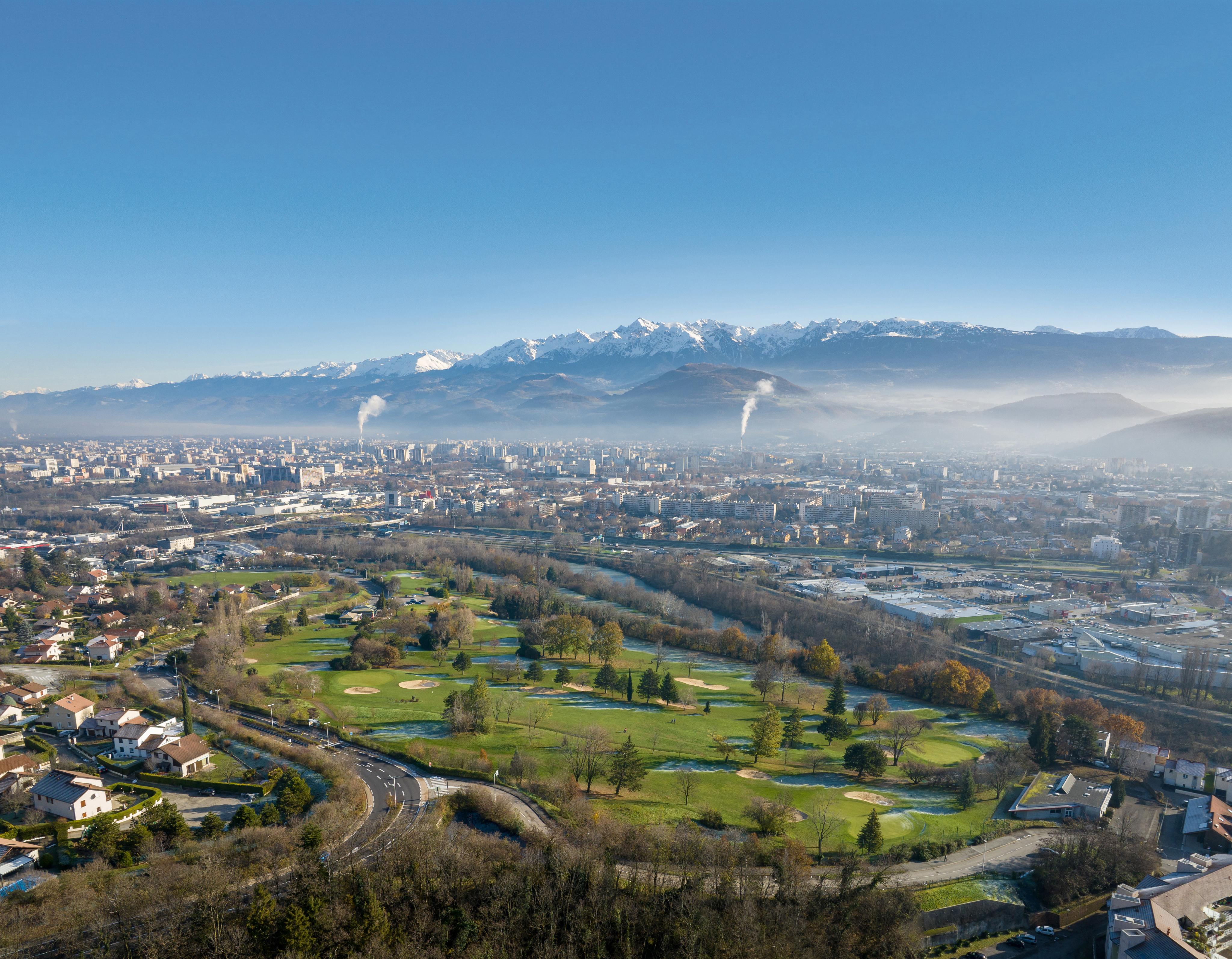 Vue panoramique d'une ville en plaine avec parcours de golf au premier plan et chaîne de montagnes enneigées en arrière-plan