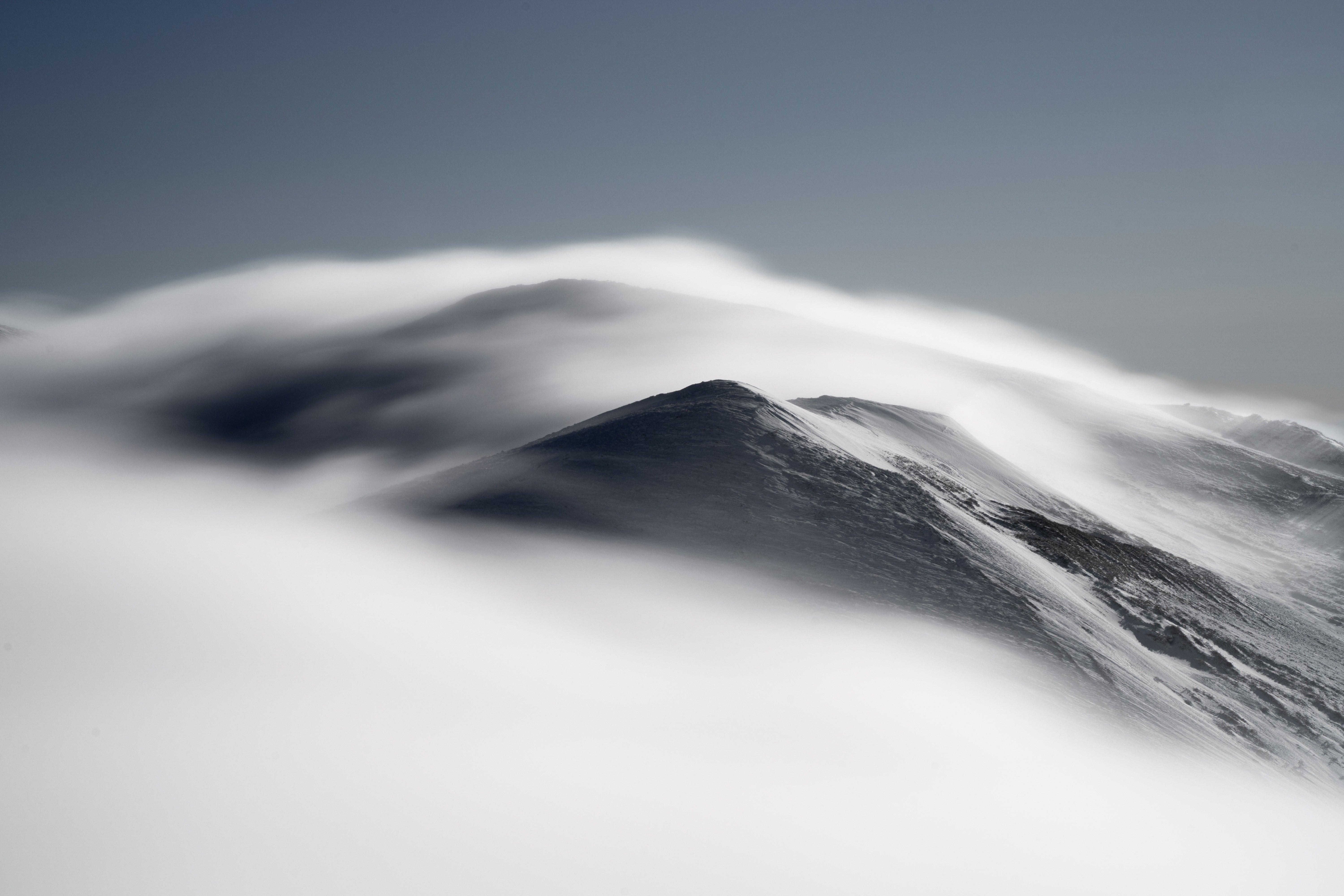 Snow-capped summit wreathed in cloud drifting along the ridge, graphic black-and-white mood