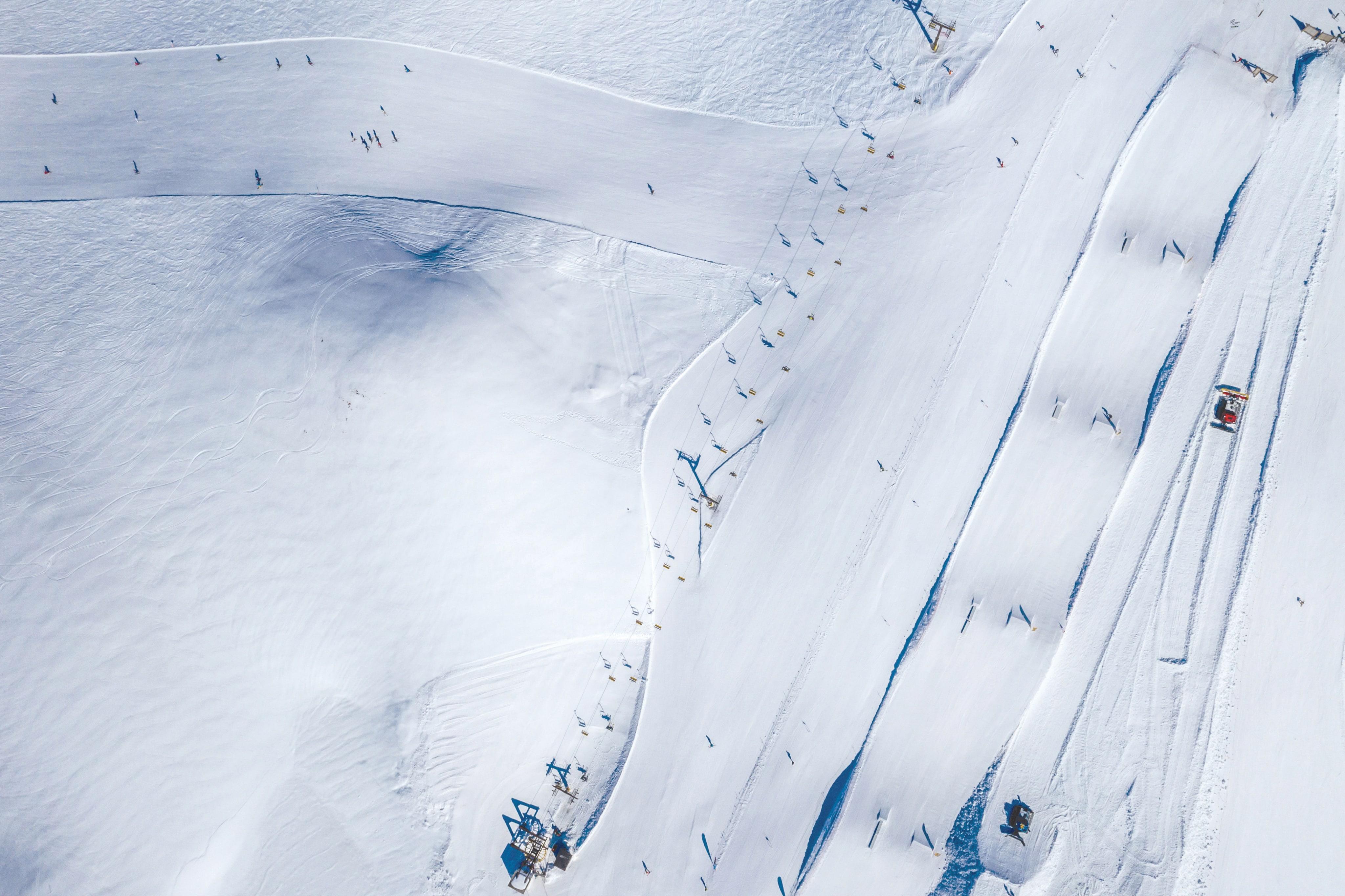Vue aérienne d'un domaine skiable enneigé avec télésièges, traces de skieurs et dameuse en action sur les pistes