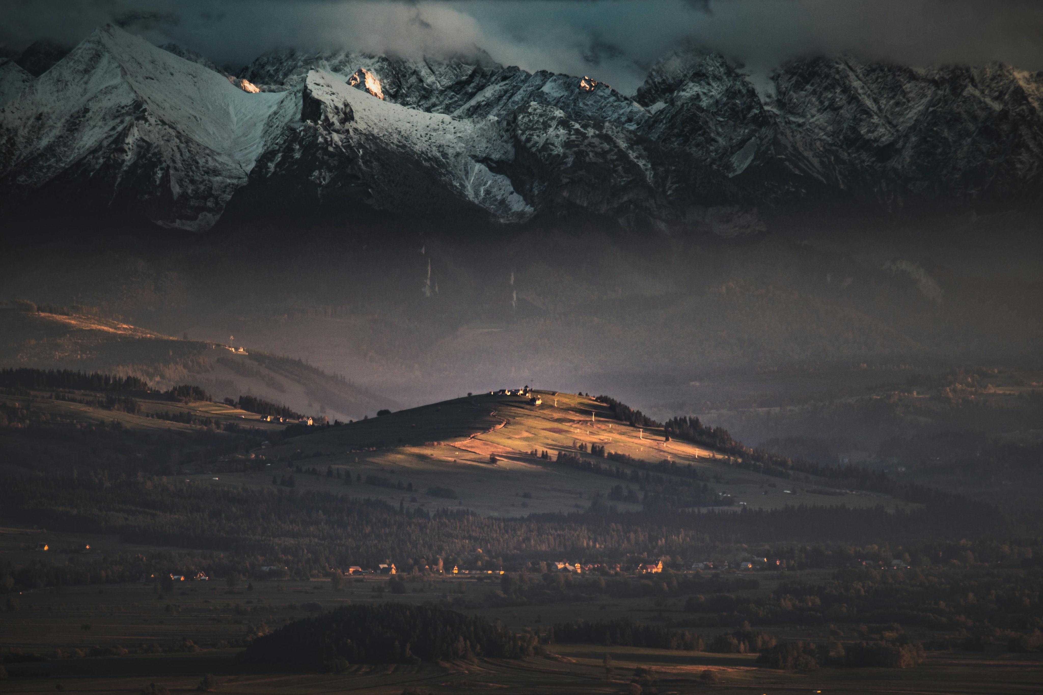 Panorama de montagnes enneigées au crépuscule, avec une colline éclairée par les derniers rayons au premier plan