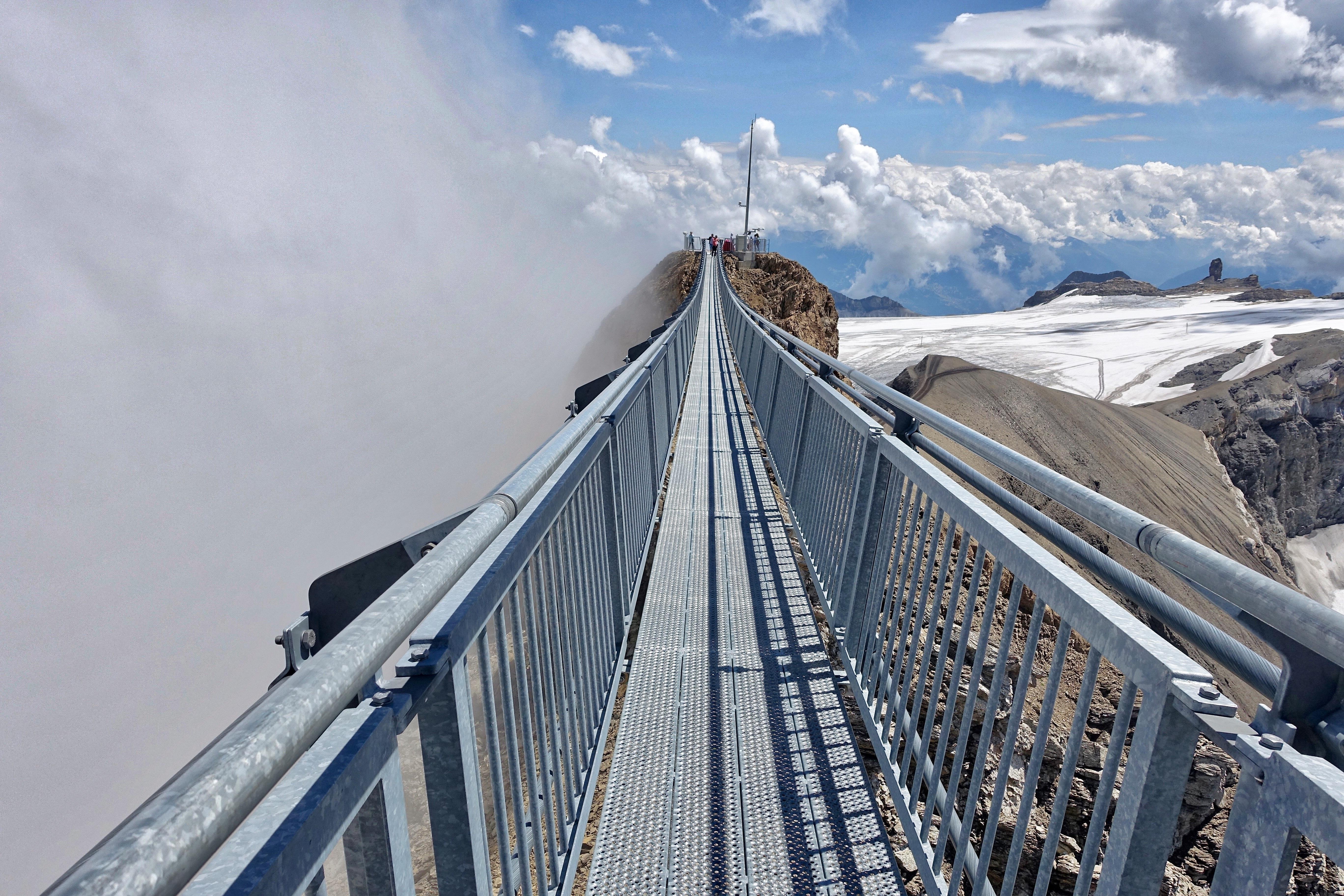 Passerelle suspendue piétonne s'avançant dans les nuages au-dessus d'un glacier alpin