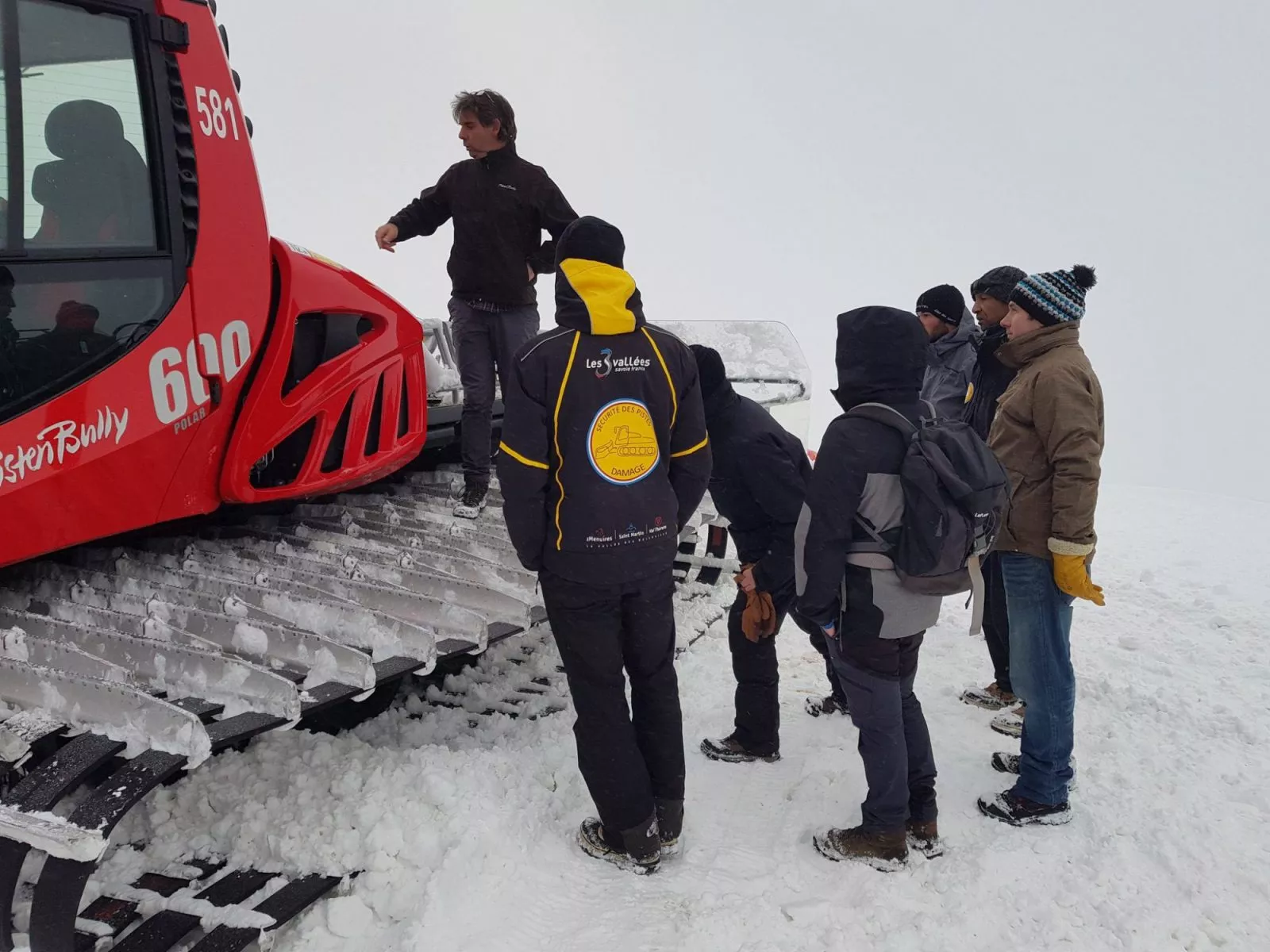 Groupe de stagiaires écoutant une présentation devant une dameuse, lors d'une formation en station