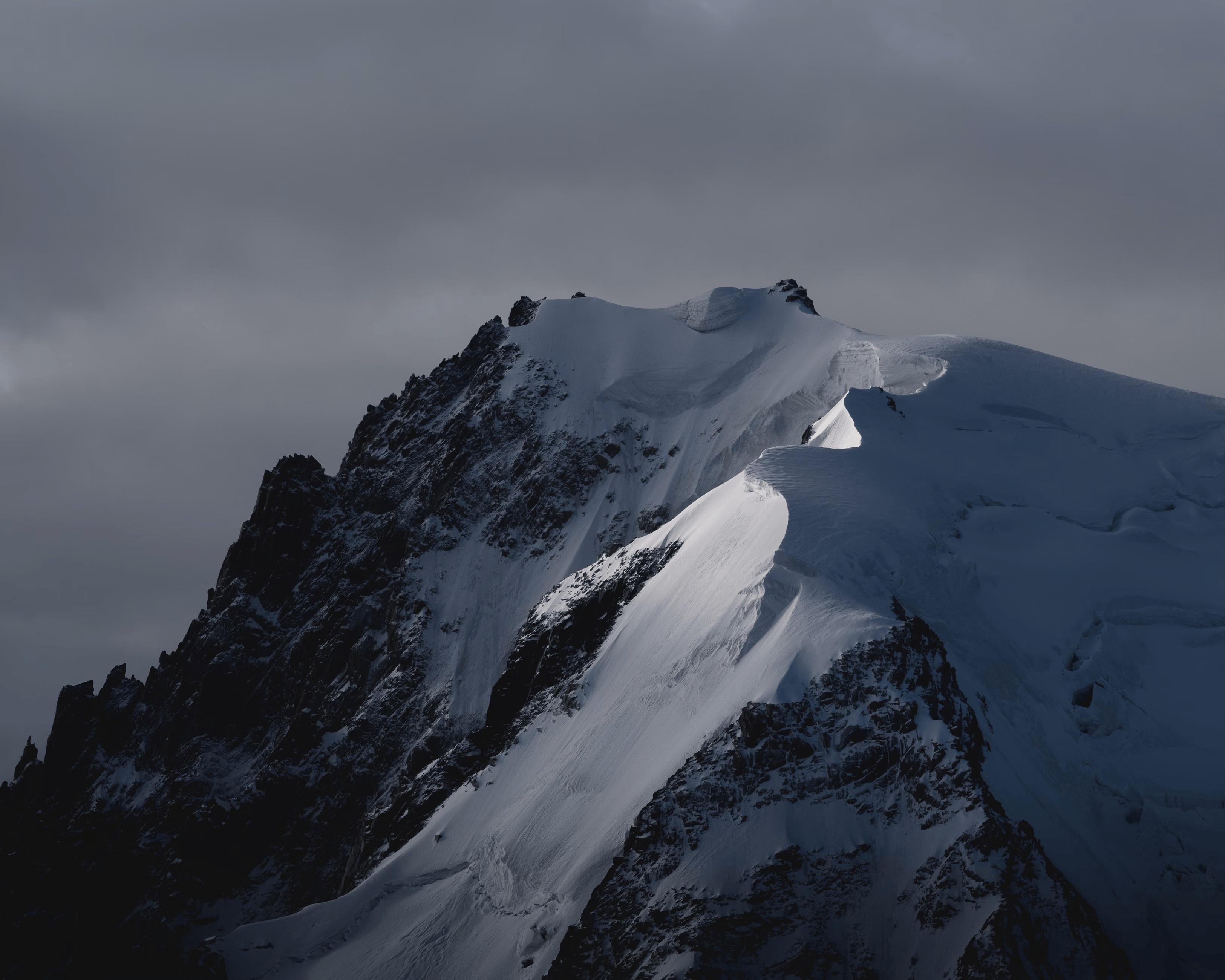 Sommet de haute montagne enneigé avec arête rocheuse et glacier, sous un ciel nuageux