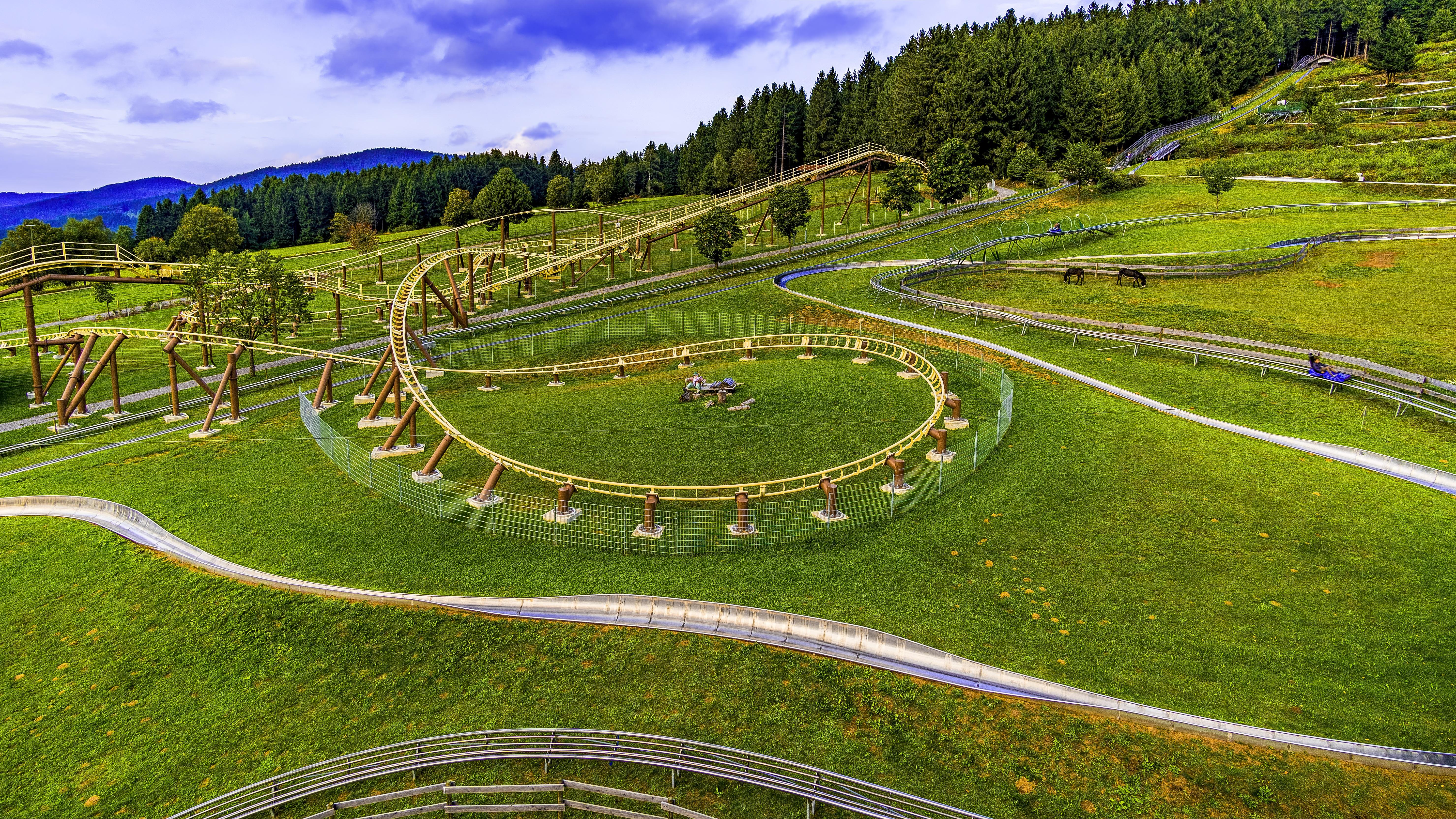 Parc de loisirs estival avec piste de luge sur rails sinueuse, au cœur de prairies vertes