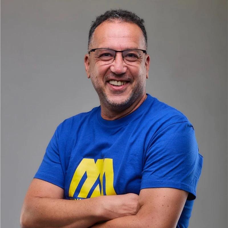 Retrato de João Ribeiro, sorridente, com óculos e camisola azul