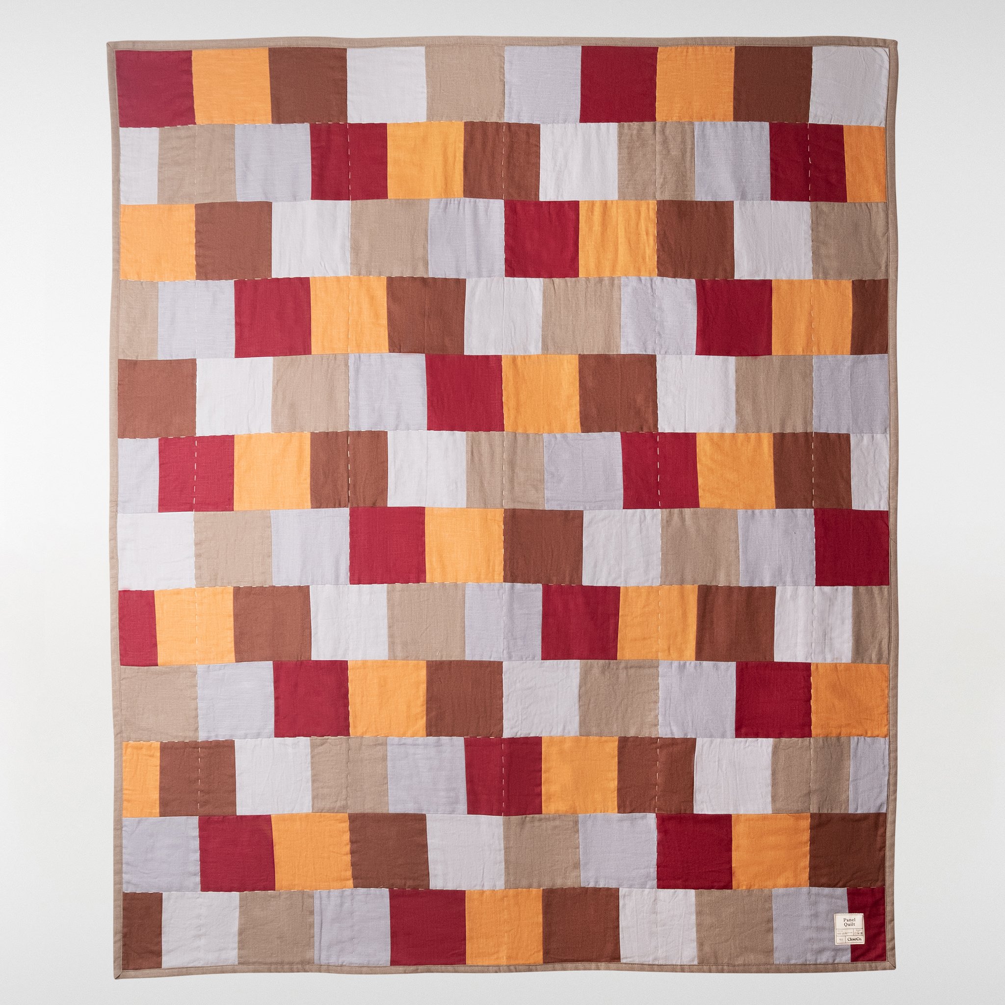 Panel patchwork quilt in warm red, rust, ochre and neutral tones, full view showing structured geometric panel design in linen and cotton