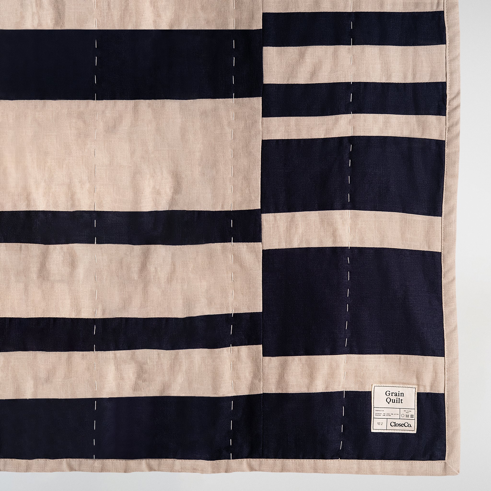 Grain patchwork quilt in navy and natural tones, close-up detail highlighting stitched stripes, fabric texture and panel construction