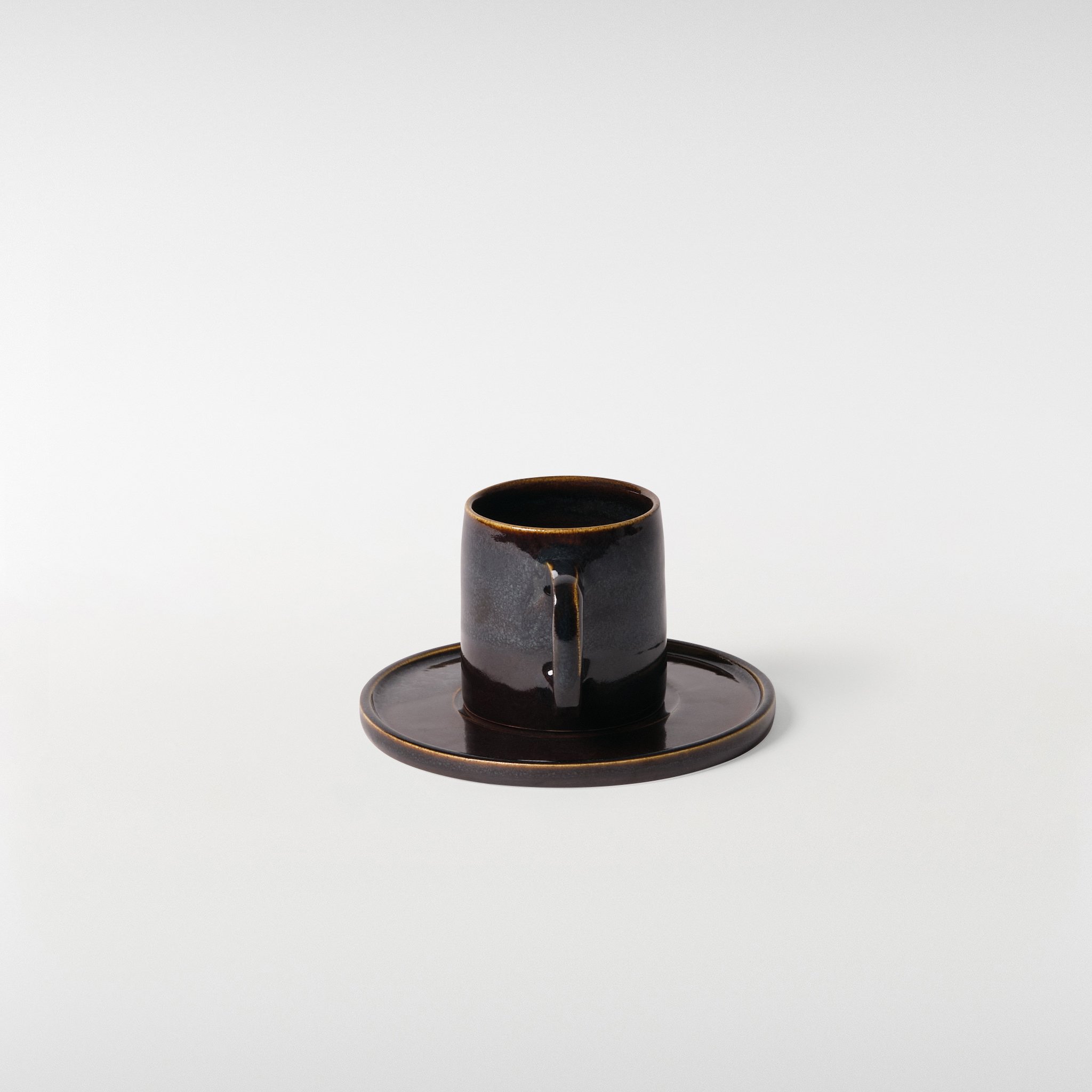 Midnight glazed ceramic cup and saucer set, rear angle showing handle shape, glaze depth and refined minimal form
