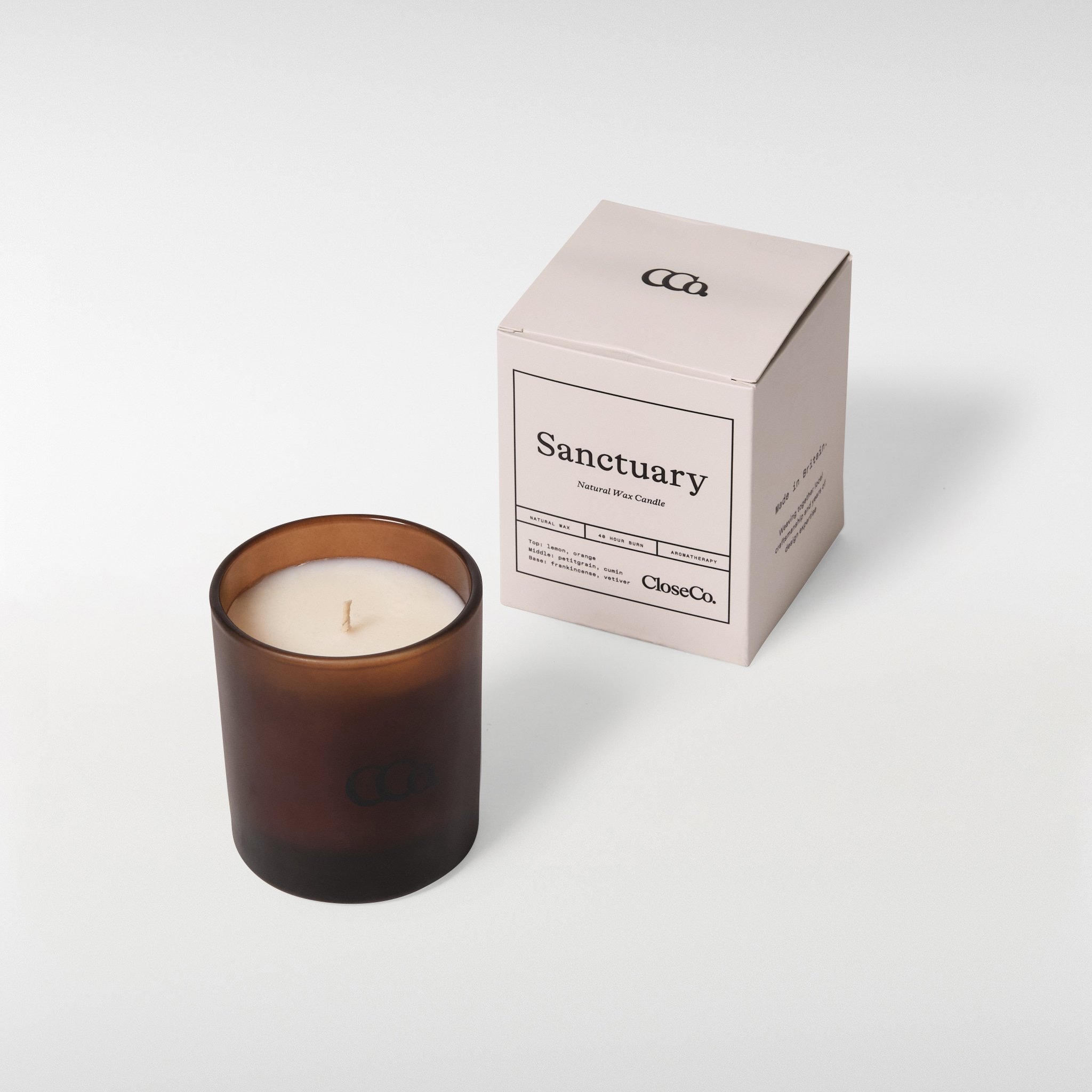 CloseCo Sanctuary candle in an amber glass vessel with a single wick, shown alongside its minimal branded box on a neutral background.