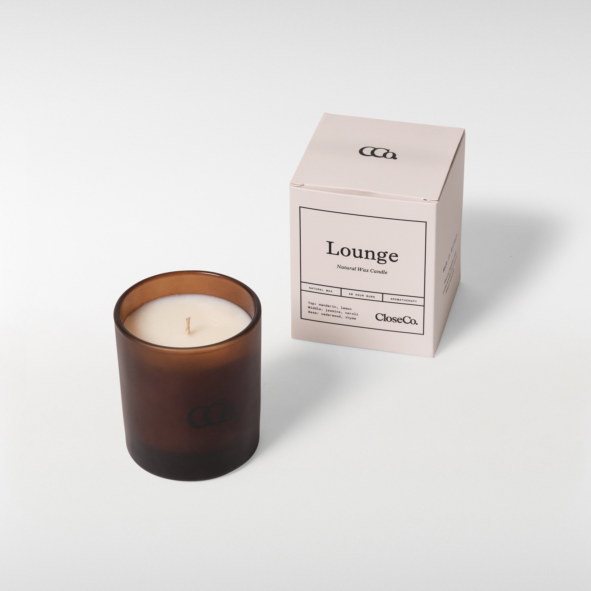 CloseCo Lounge candle in an amber glass vessel with a single wick, shown alongside its minimal branded box on a neutral background.