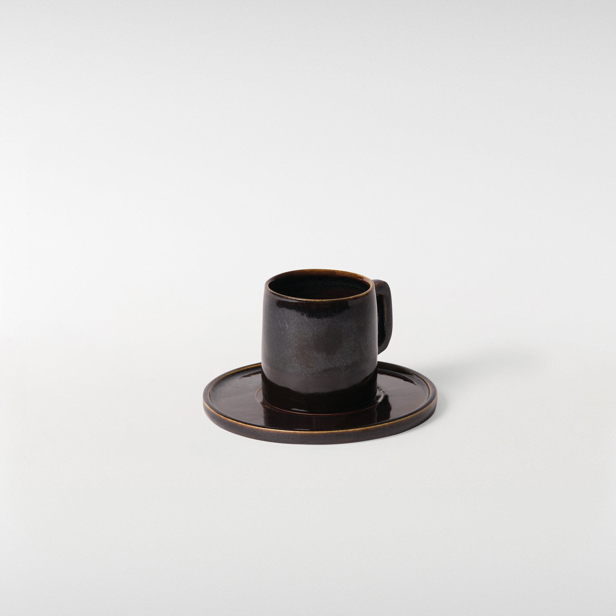 Midnight glazed ceramic cup and saucer set, side angle highlighting structured silhouette, handle detail and smooth circular saucer