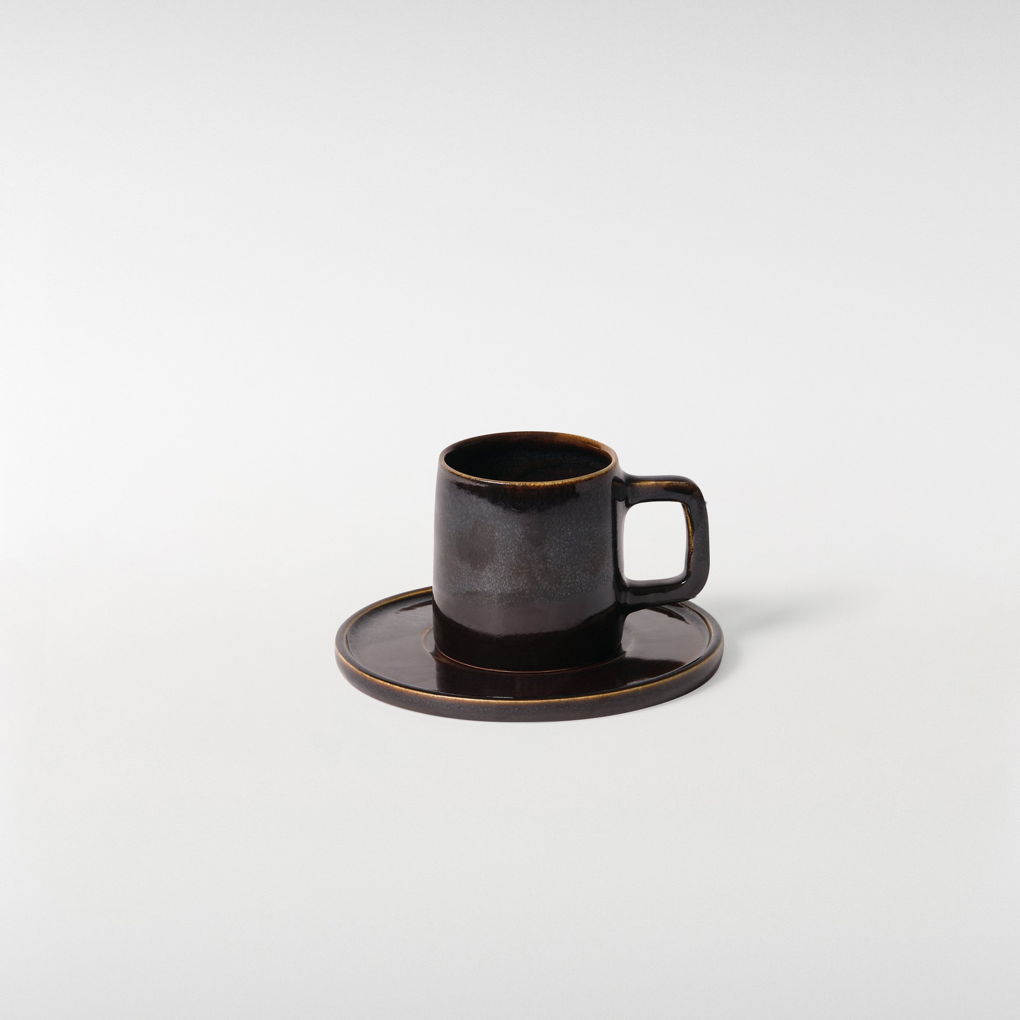 Midnight glazed ceramic cup and saucer set, front angle showing clean cylindrical form, squared handle and subtle tonal glaze variation