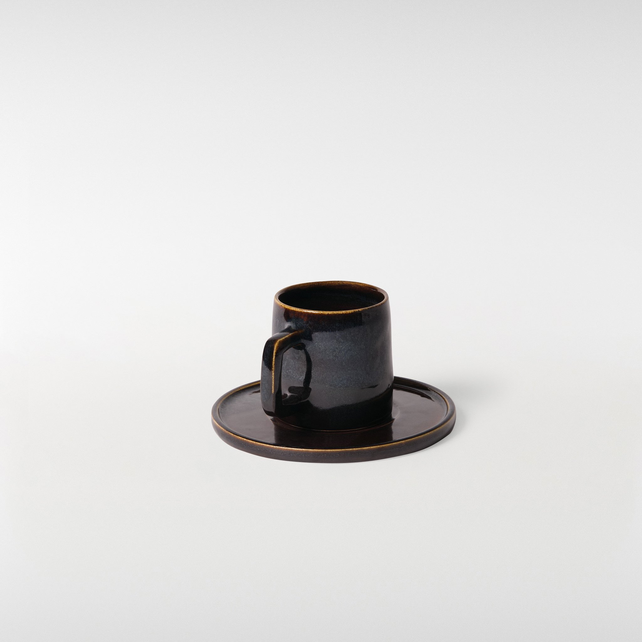 Midnight glazed ceramic cup and saucer set, three-quarter view emphasising sharp lines, quiet tonal shifts and balanced proportions