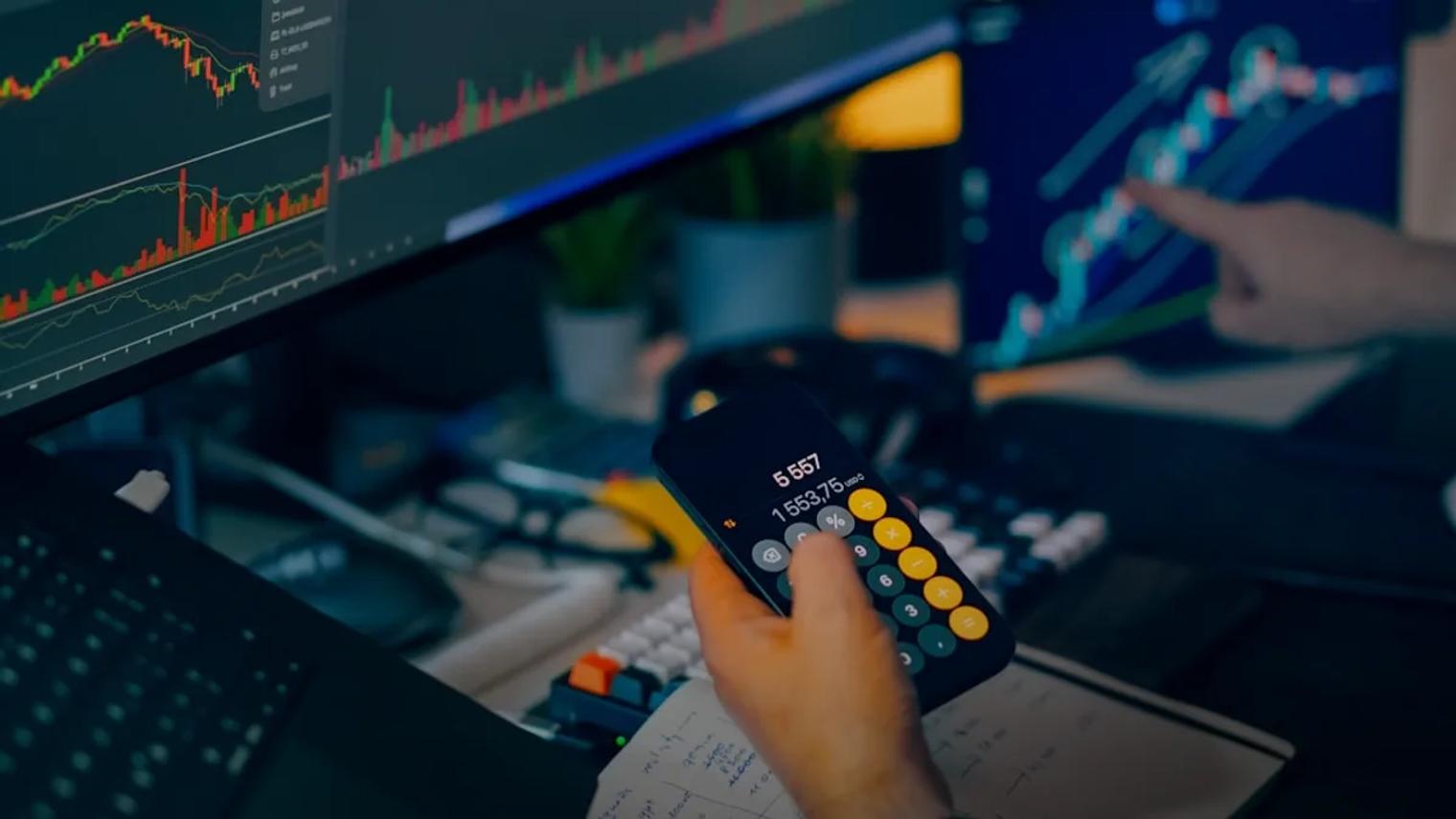 Trader analyzing stock market charts on computer screens with calculator