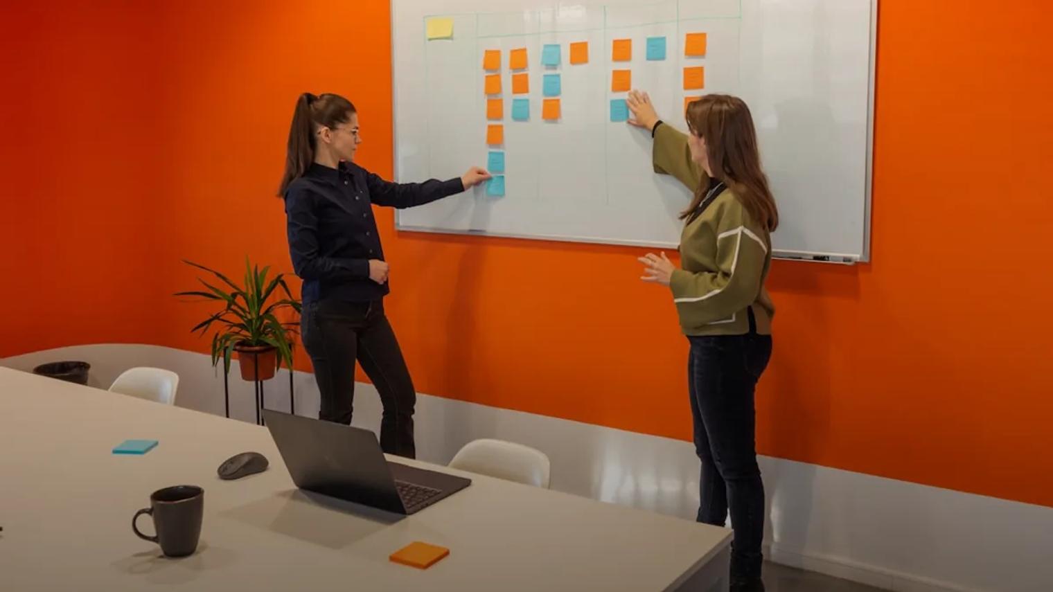 two women standing in front of a white board