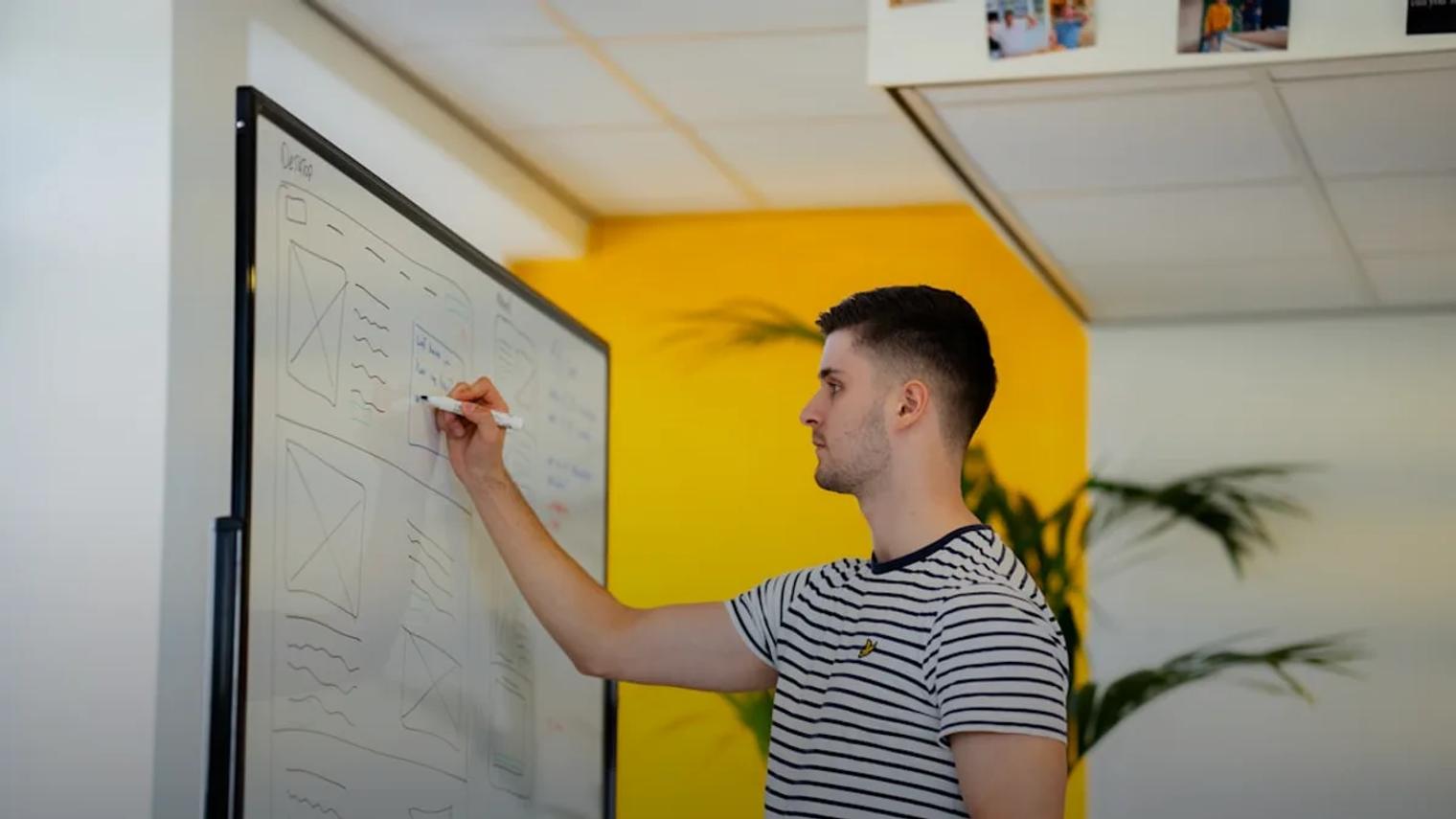 a man standing in front of a whiteboard writing on it