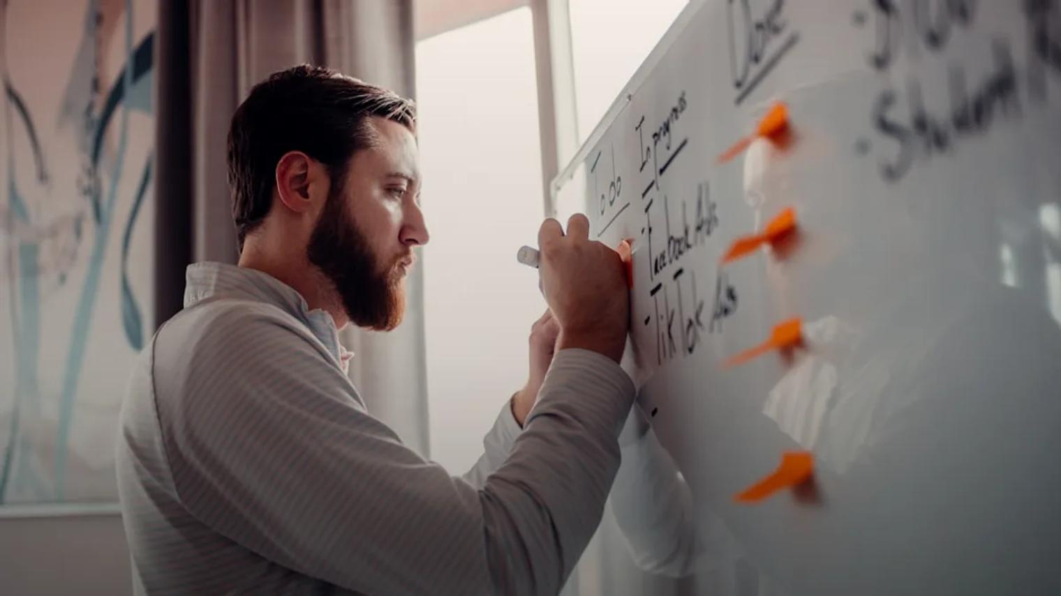 a man writing on a white board with orange markers