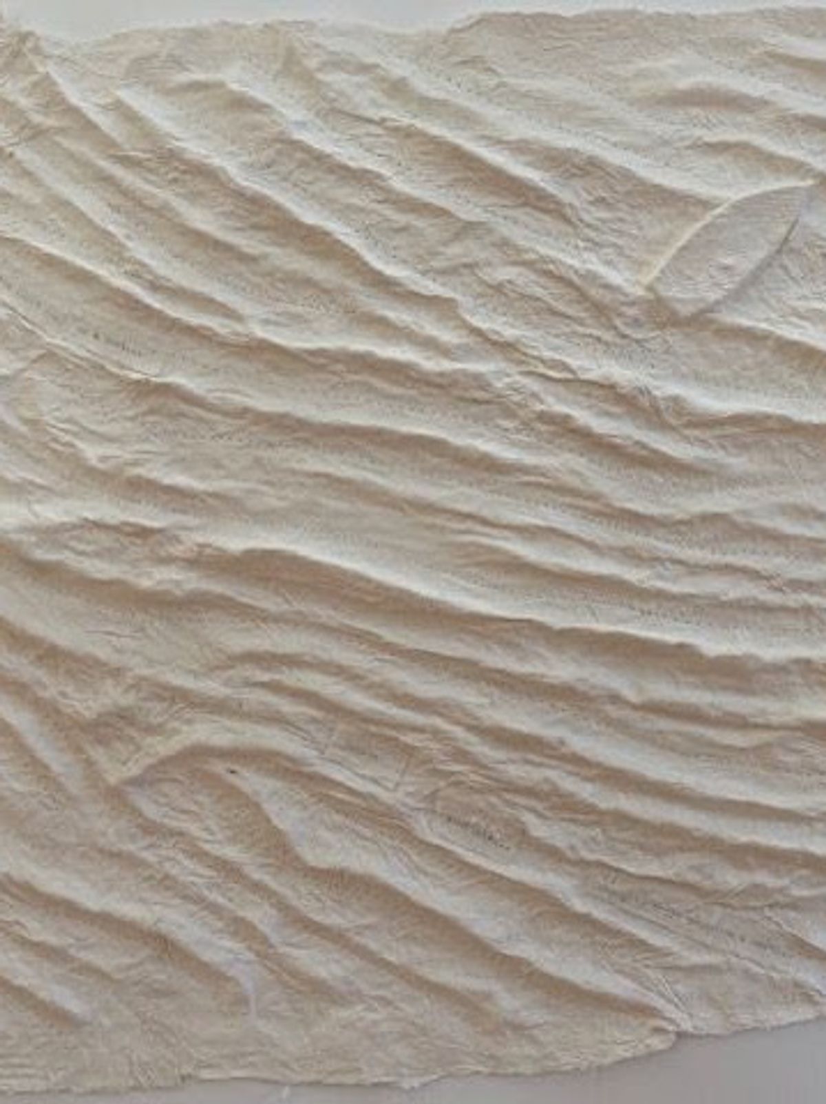A large sheet of cream handmade paper crumpled into deep horizontal ridges, reading like wind-rippled sand or slow water. Faint impressed marks catch in the troughs; one corner lifts free.