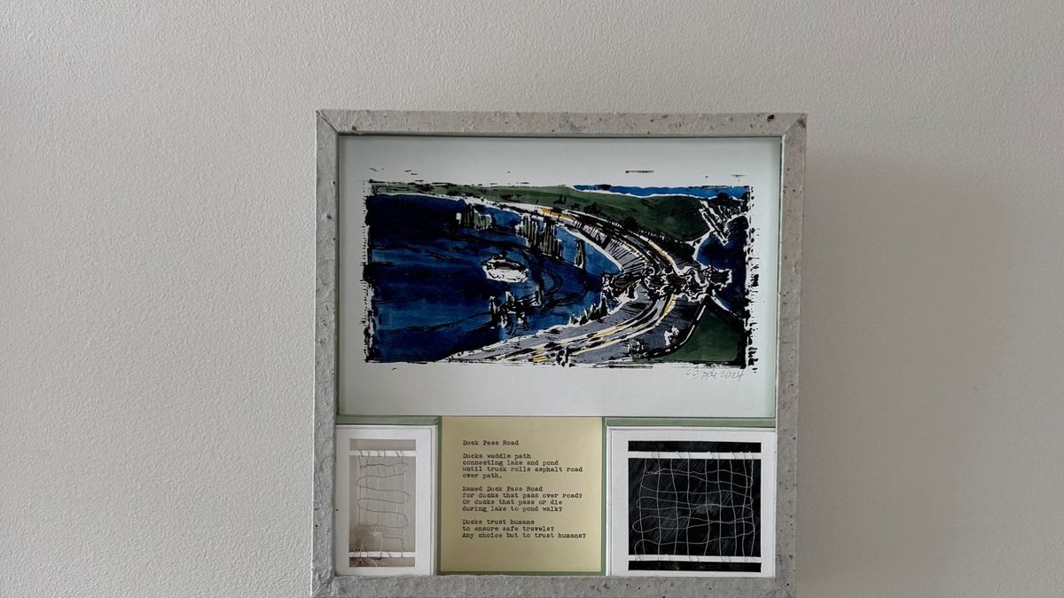 A grey speckled handmade-paper frame holds a vivid blue ink and wash landscape of a curving road beside water. Below it a typed poem on ochre paper sits between two small windows containing pale threads and dark netting.