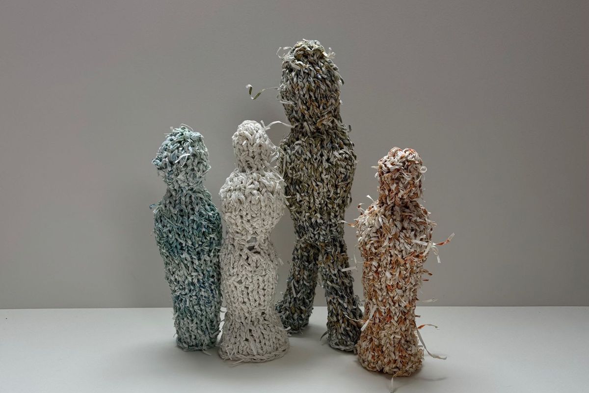 Four standing figures knitted from twisted paper cord, in teal, cream, mottled olive and rust. Loose paper ends bristle from every surface. They stand together on white, the tallest looking slightly upward.