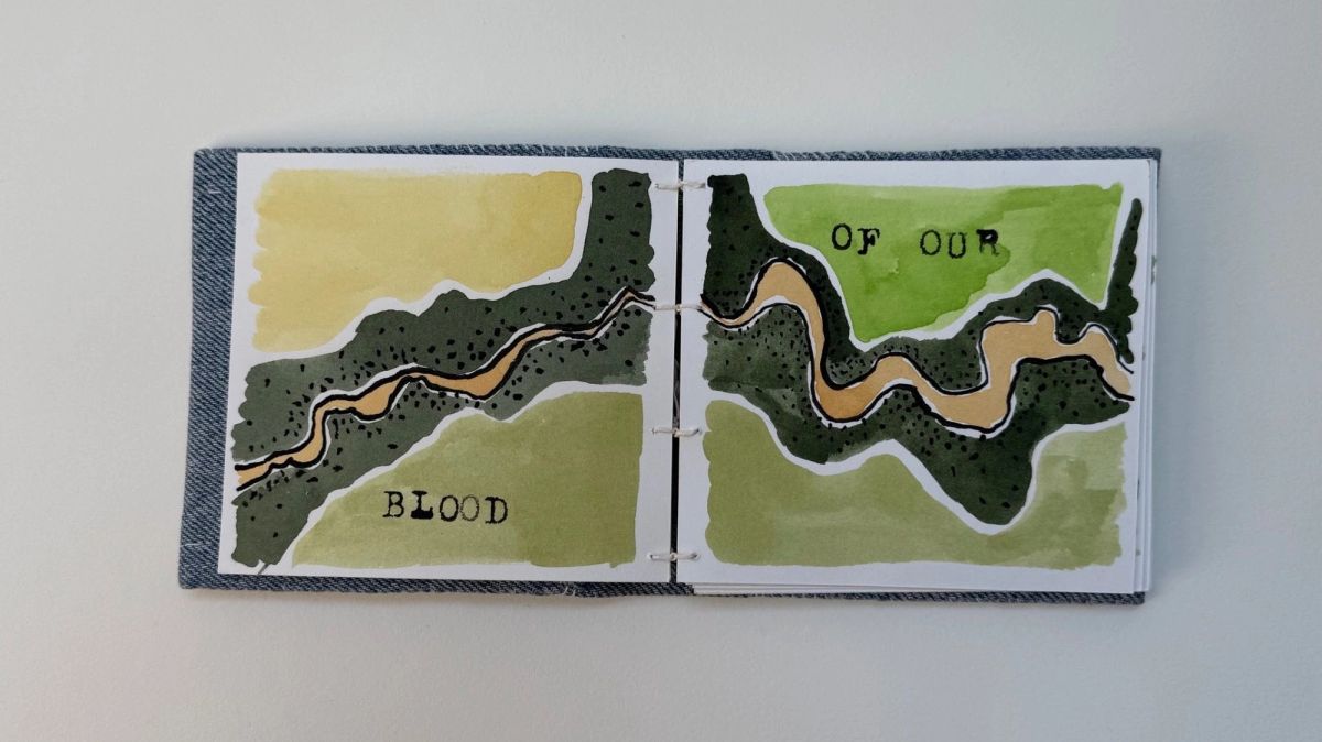 An open book with pale denim covers. Both pages carry an aerial river map in olive and moss with a tan channel winding through, stamped with the words "BLOOD" and "OF OUR".