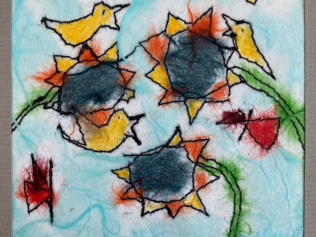 A felted panel on white and aqua wool, machine-stitched in black outline. Three sunflowers with dense grey centres and orange-yellow petals, circled by yellow birds and two crimson butterflies.