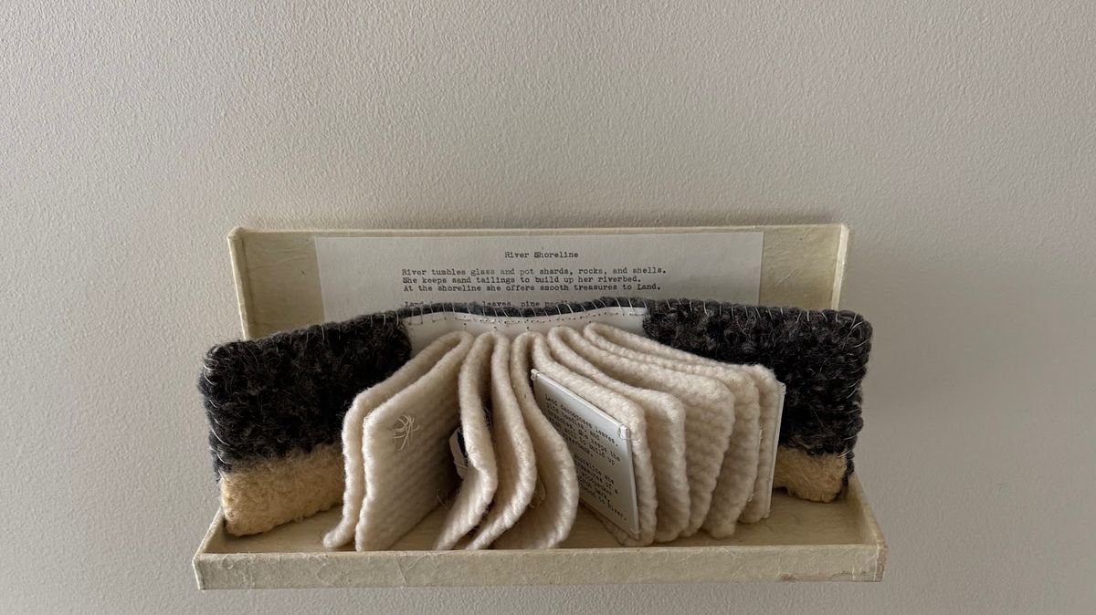 A cream box holds a typed poem behind a fan of thick knitted cream pages, flanked by two dense charcoal boucle-textured blocks. Small printed slips are tucked between the ribbed pages.