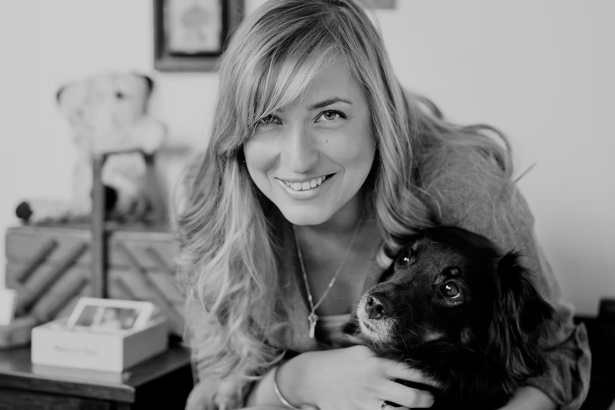Black and white portrait of designer Rafaela Kalderon smiling, holding a small dog