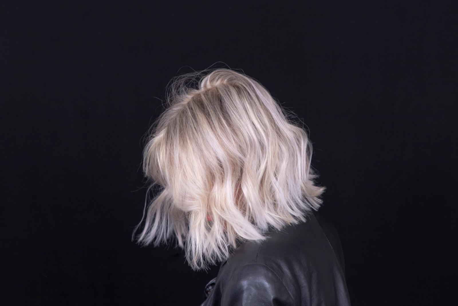 Woman with short platinum blonde hair fencing to the side while looking down with a black background.