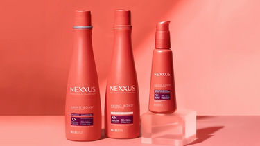 The entire Nexxus Amino Bond Repair System collection and two scientific beakers are shown against a peachy orange background.