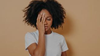 Woman with white t-shirt standing with right hand lifted to her forehead, covering half of her face.