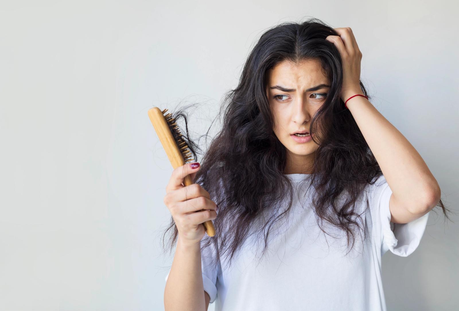 Woman with black wavy hair looking shocked as brushing hair a chunk of her hair comes off.