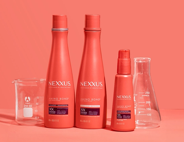 The entire Nexxus Amino Bond Repair System collection and two scientific beakers are shown against a peachy orange background.