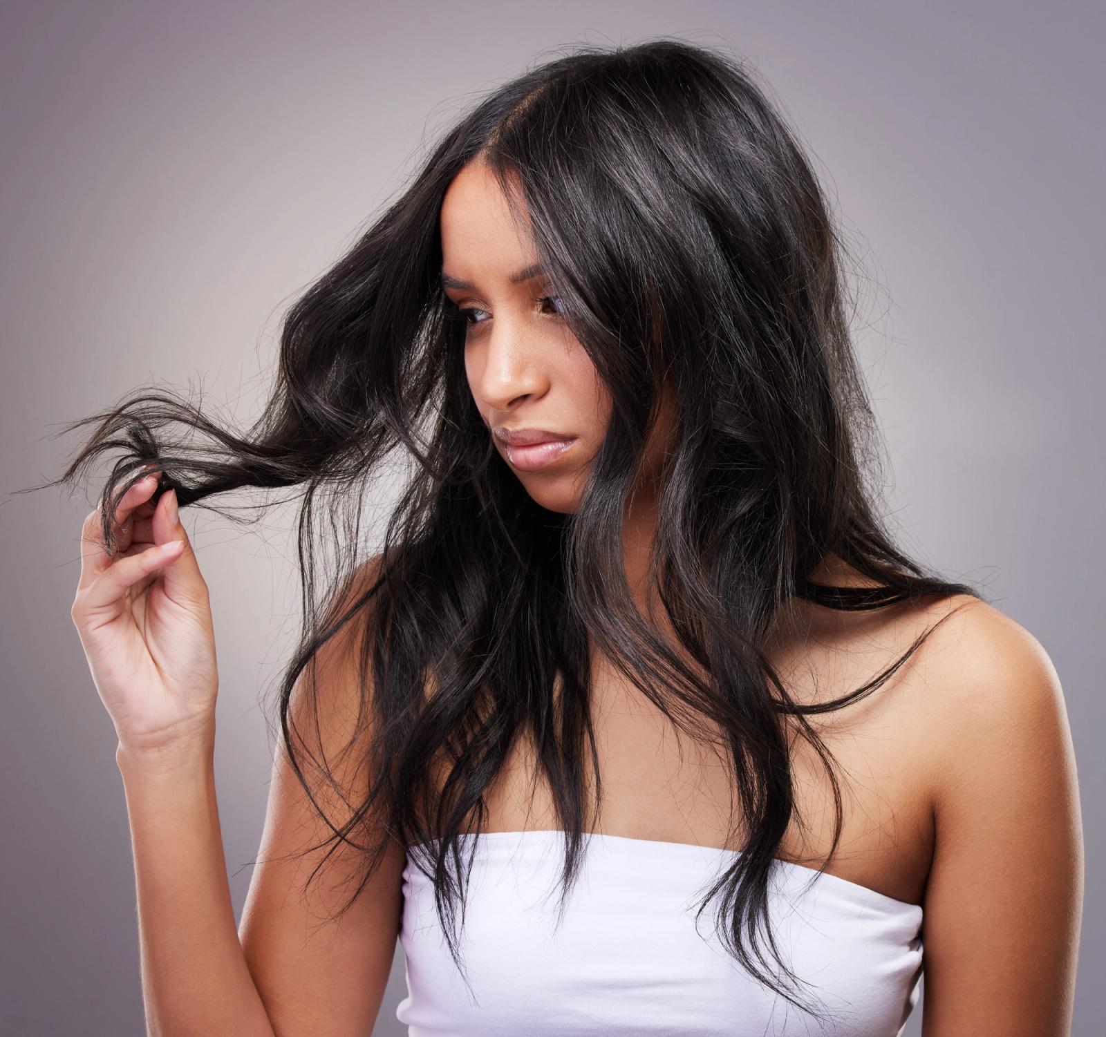 Woman with dark hair holding up the ends of her hair, looking at hair with disgust.